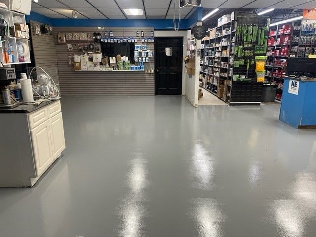 Brightly lit retail store interior with gray flooring, shelves of products, and counter space.