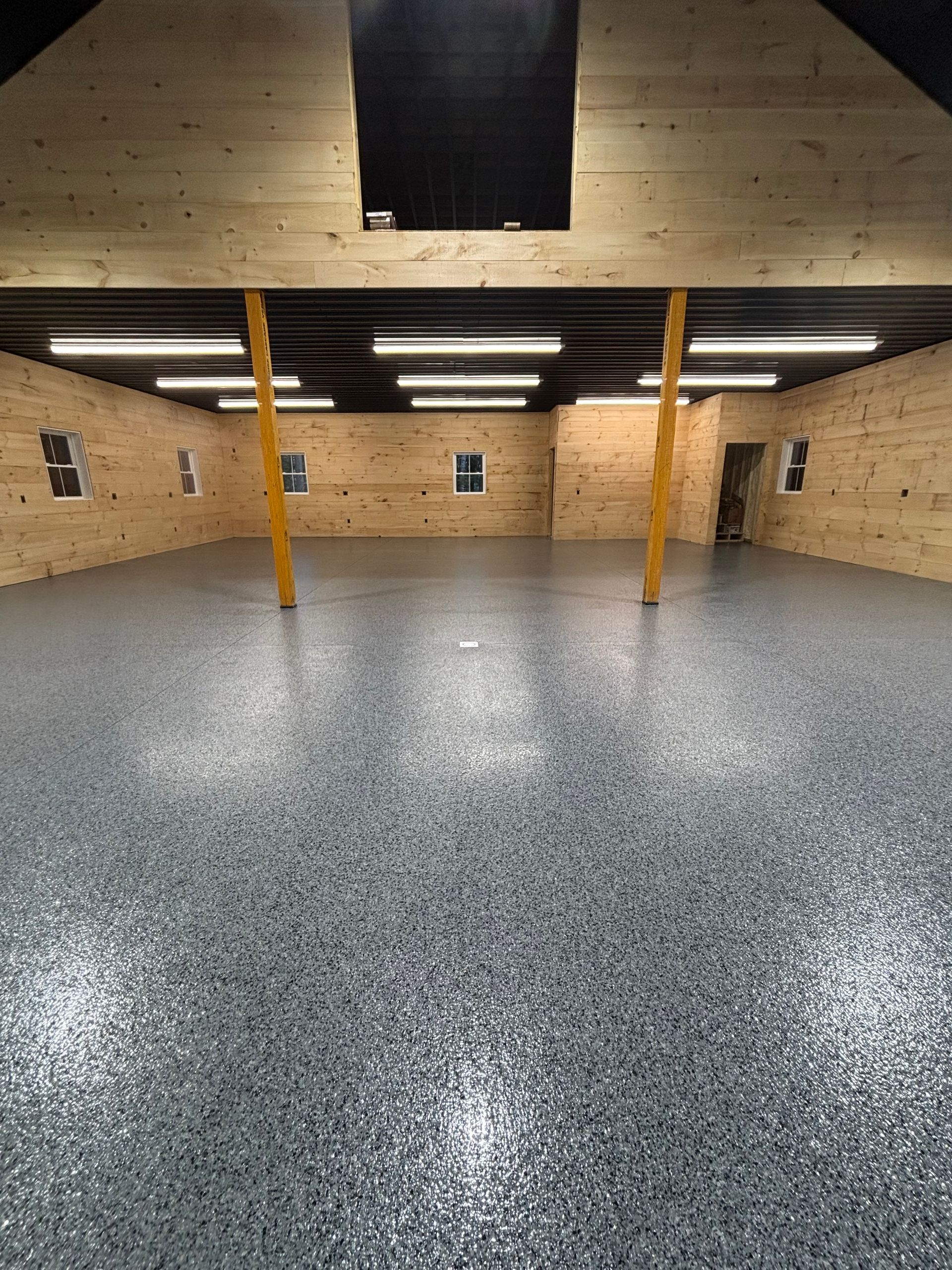 Spacious interior of a building with a speckled gray epoxy floor, wood walls, and yellow support beams.