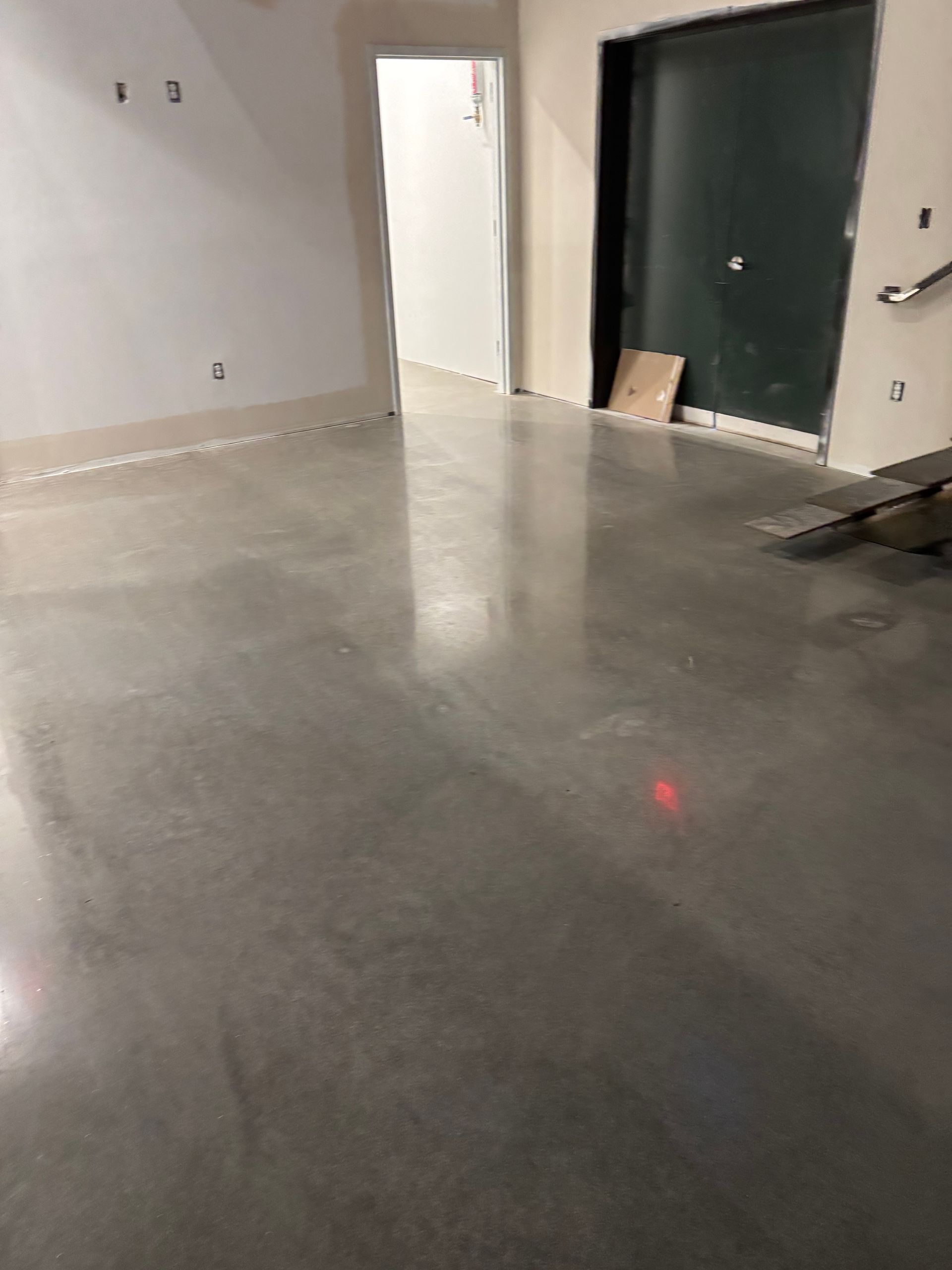 A polished concrete floor in a room with white walls, an open doorway, and a dark green door.