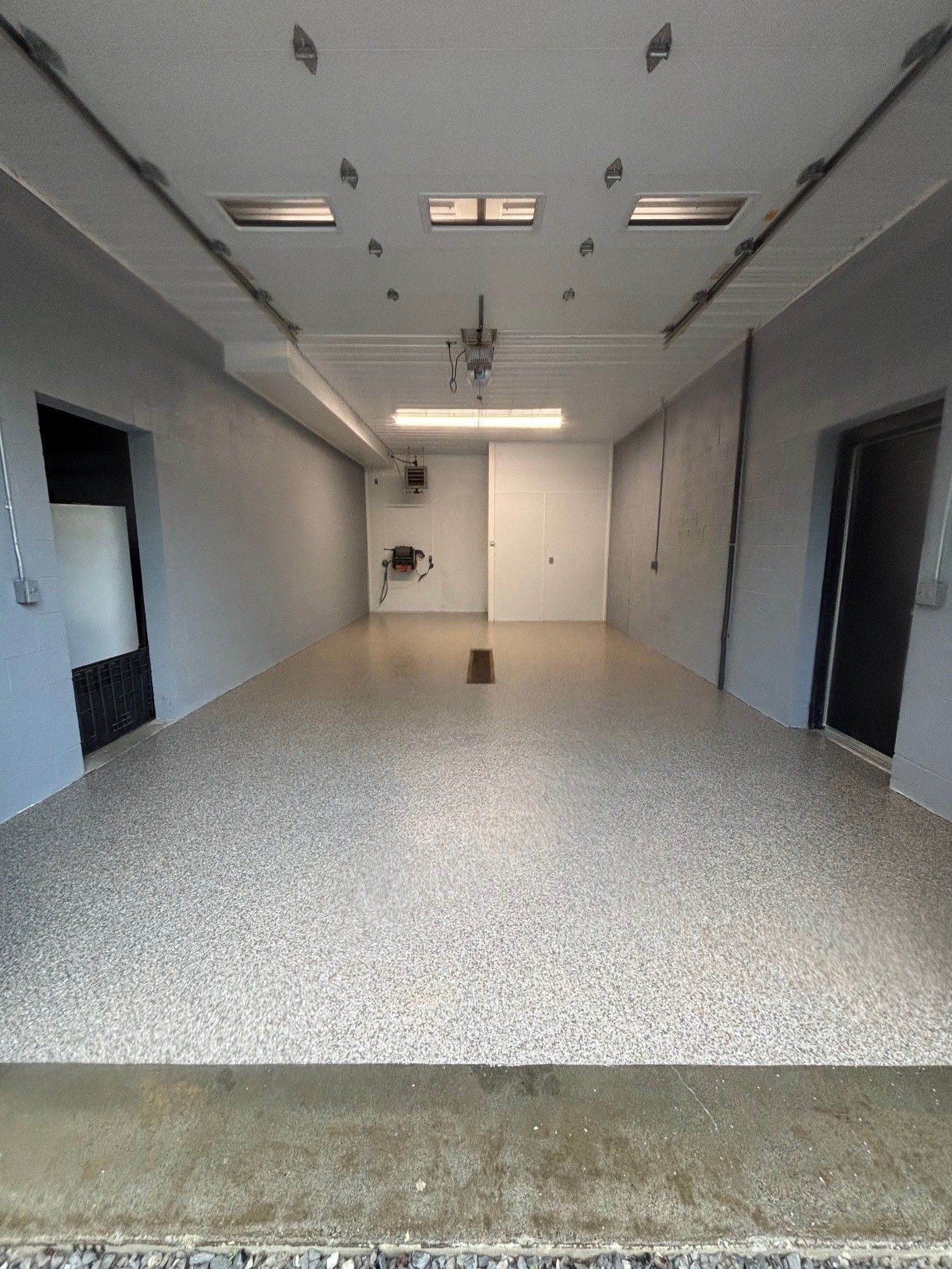 Empty art gallery interior with gray speckled floor, white walls, and bright overhead lights.