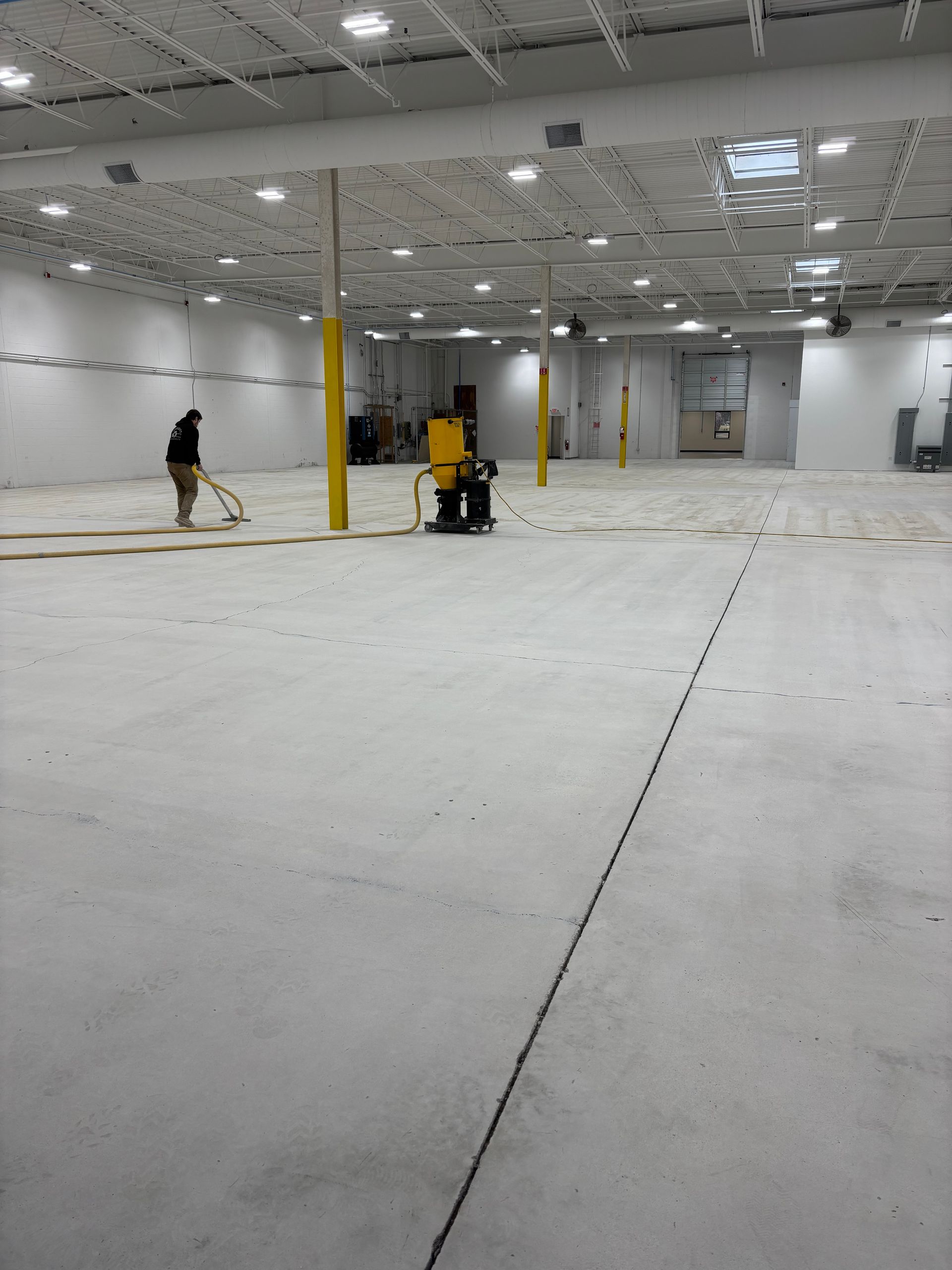 Large empty warehouse with a person cleaning the floor with machinery. The floor is light grey.