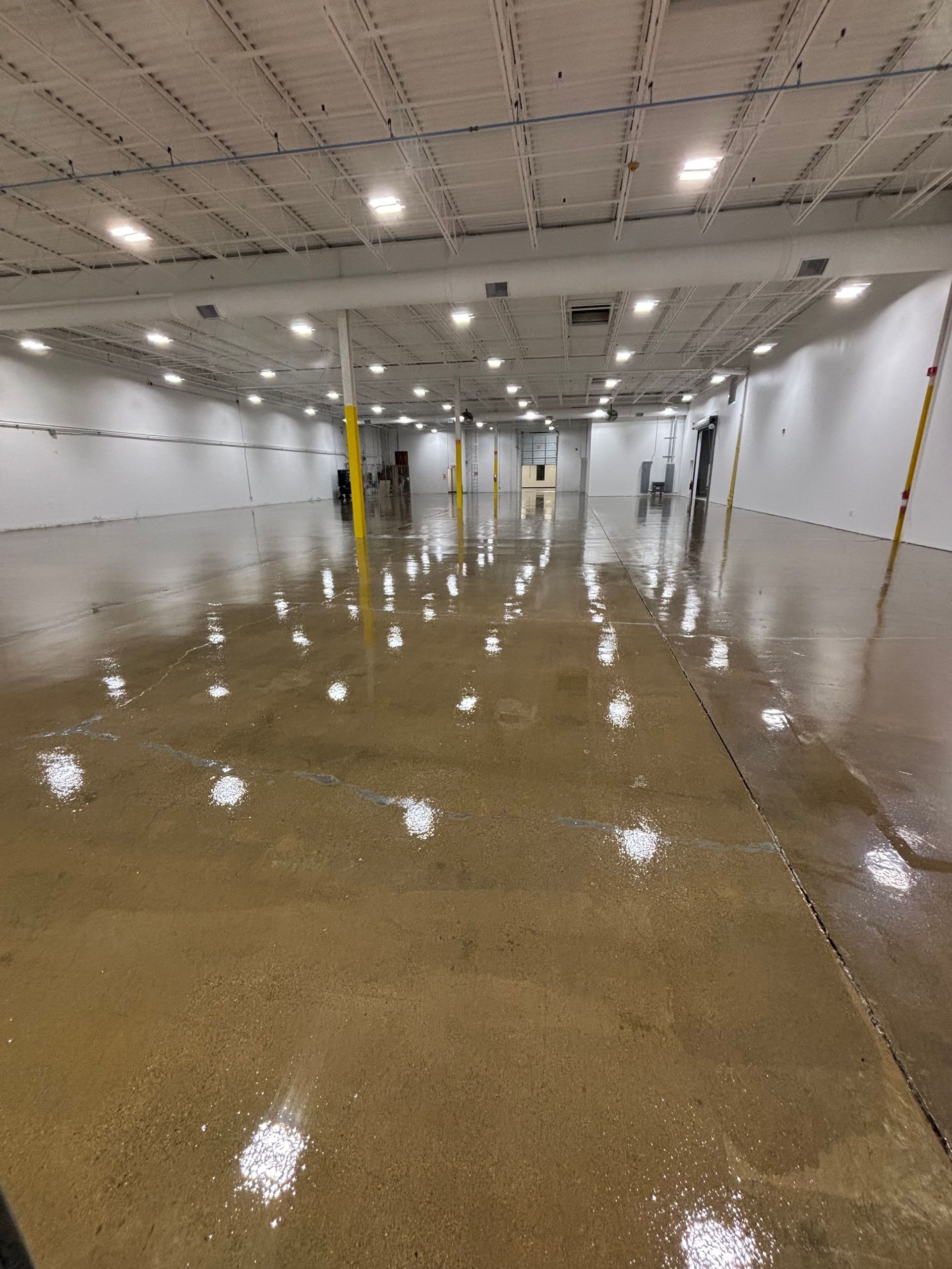 Large, empty warehouse interior with glossy concrete floor reflecting overhead lights.
