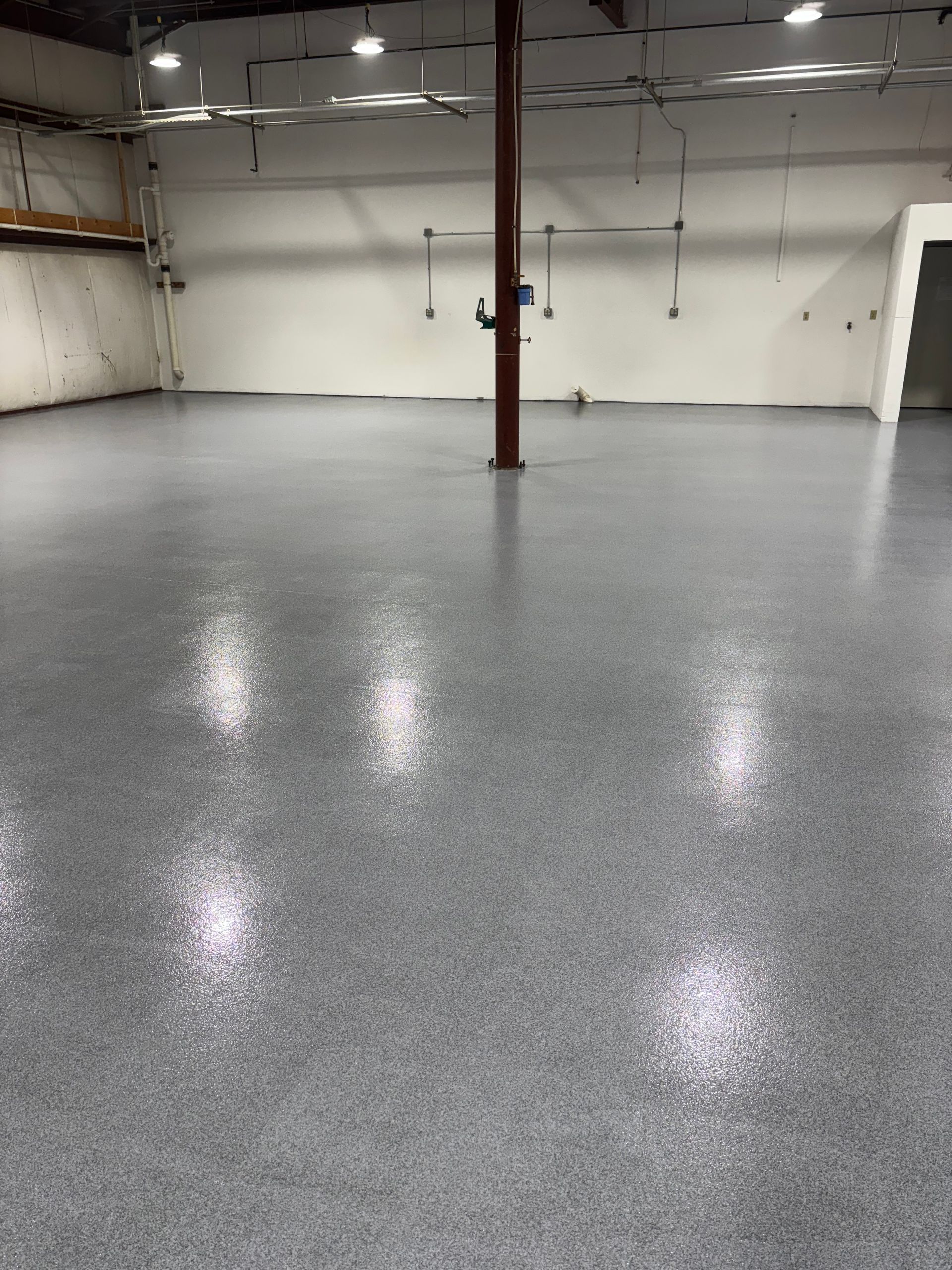 An empty warehouse with a gray speckled epoxy floor and a central brown support beam.