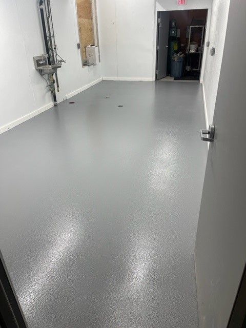 Empty room with gray epoxy floor, white walls, and a door at the end of a hallway.