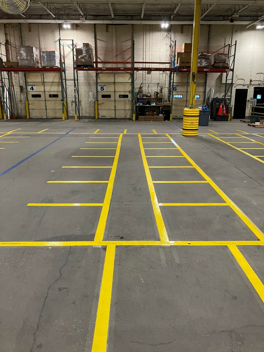Yellow floor markings in a warehouse, defining lanes and designated areas on gray concrete.