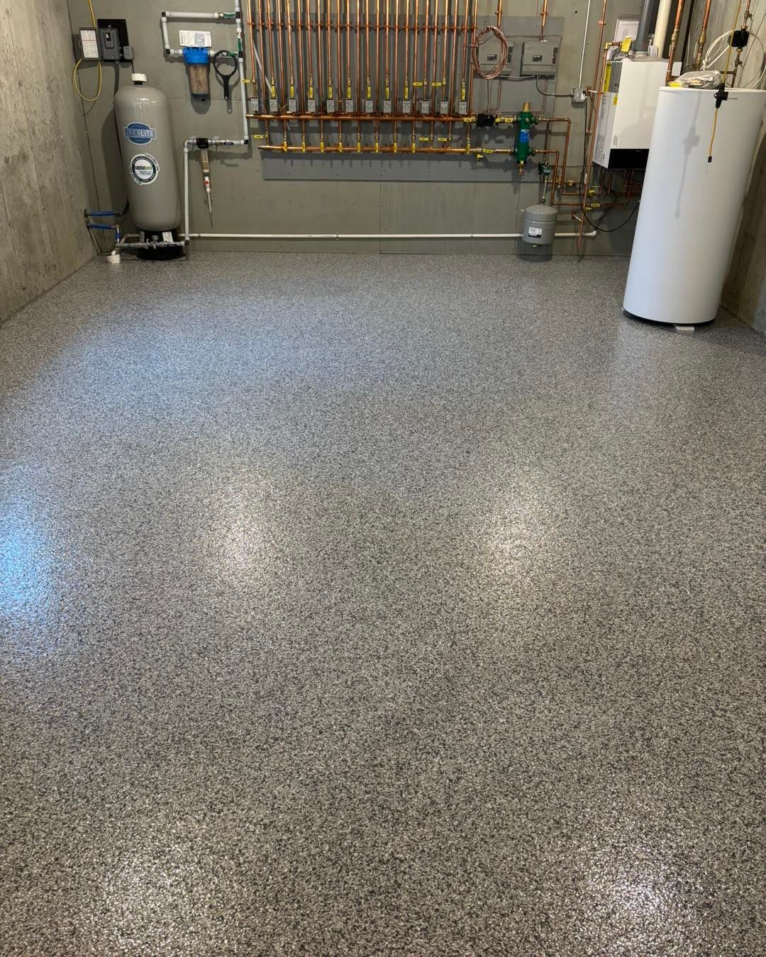 Gray speckled epoxy floor in a utility room with copper pipes and equipment.