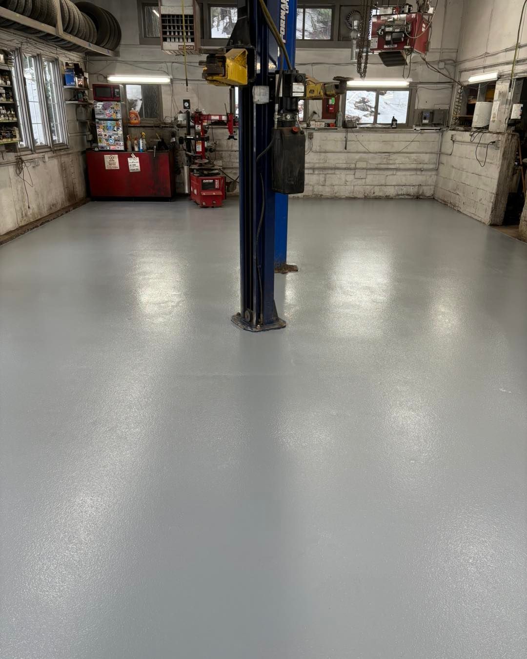 A freshly painted light gray floor in an auto repair shop with a car lift in the center.