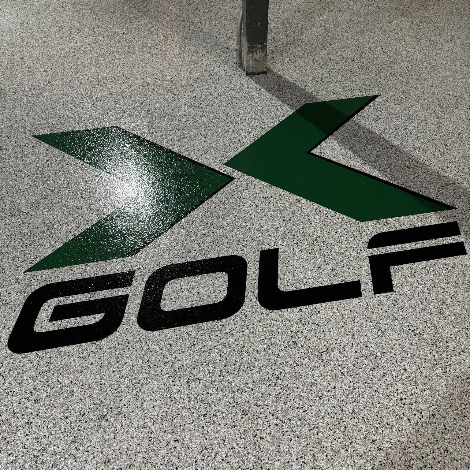 X Golf logo in green and black on speckled gray garage floor.