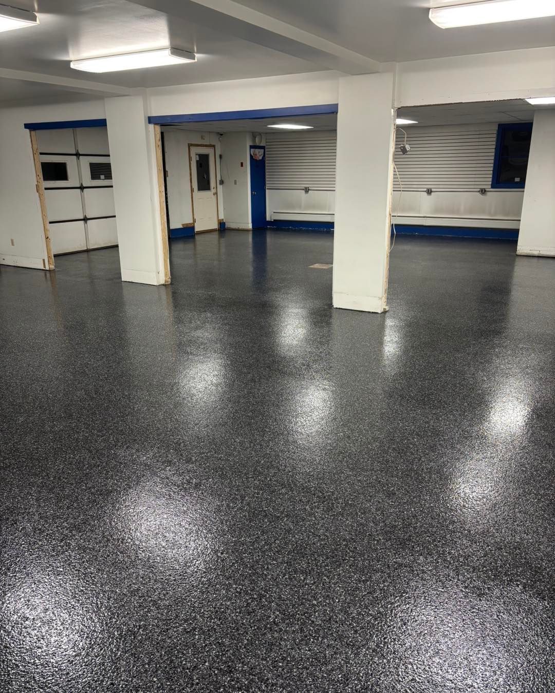 Gray speckled epoxy floor in a large, empty room with white pillars and garage doors.