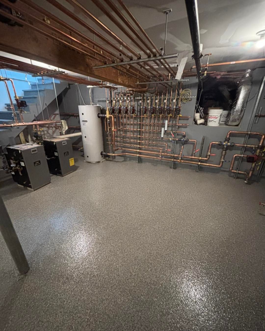 Basement mechanical room with copper pipes, a white water heater, and a gray epoxy floor.