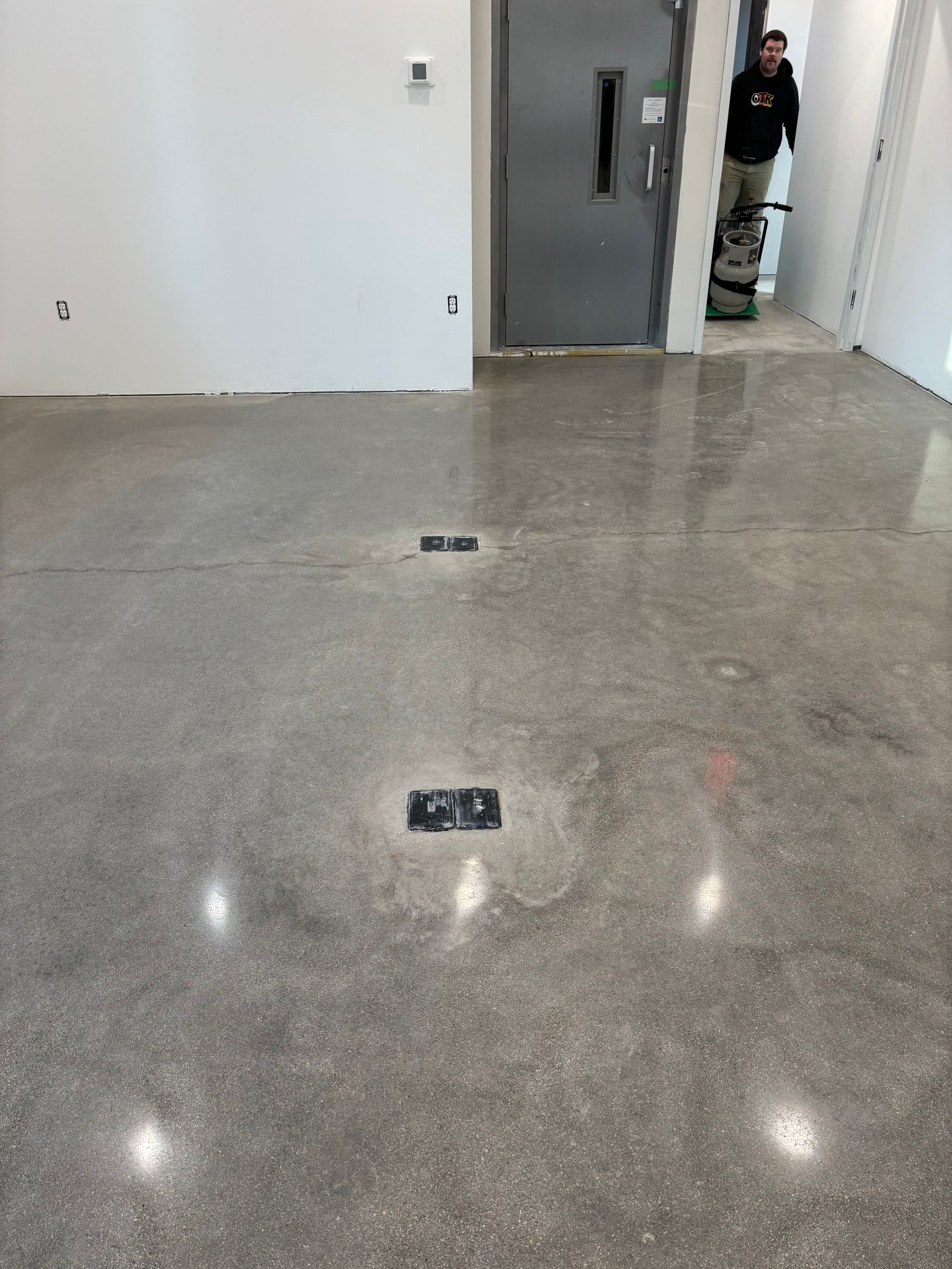 Polished concrete floor with two floor outlets; a person using a floor polishing machine near a door.