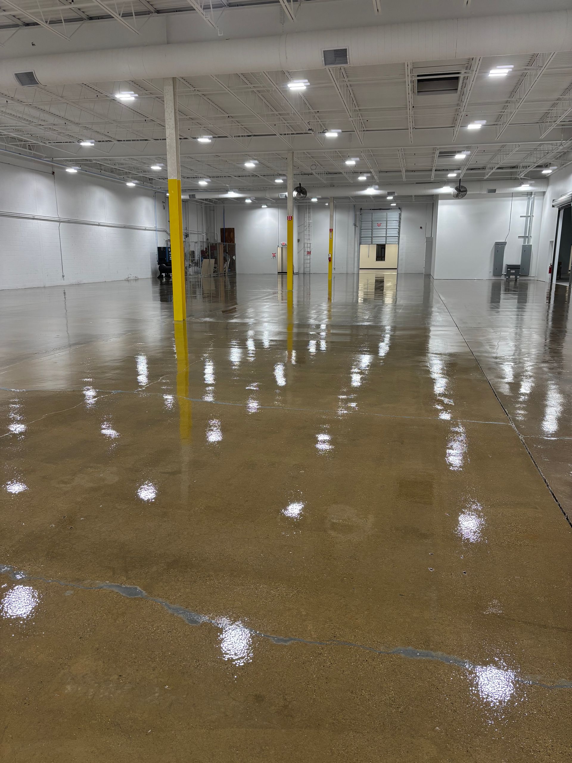 Large, empty warehouse interior with polished concrete floor, overhead lights, and yellow support beams.