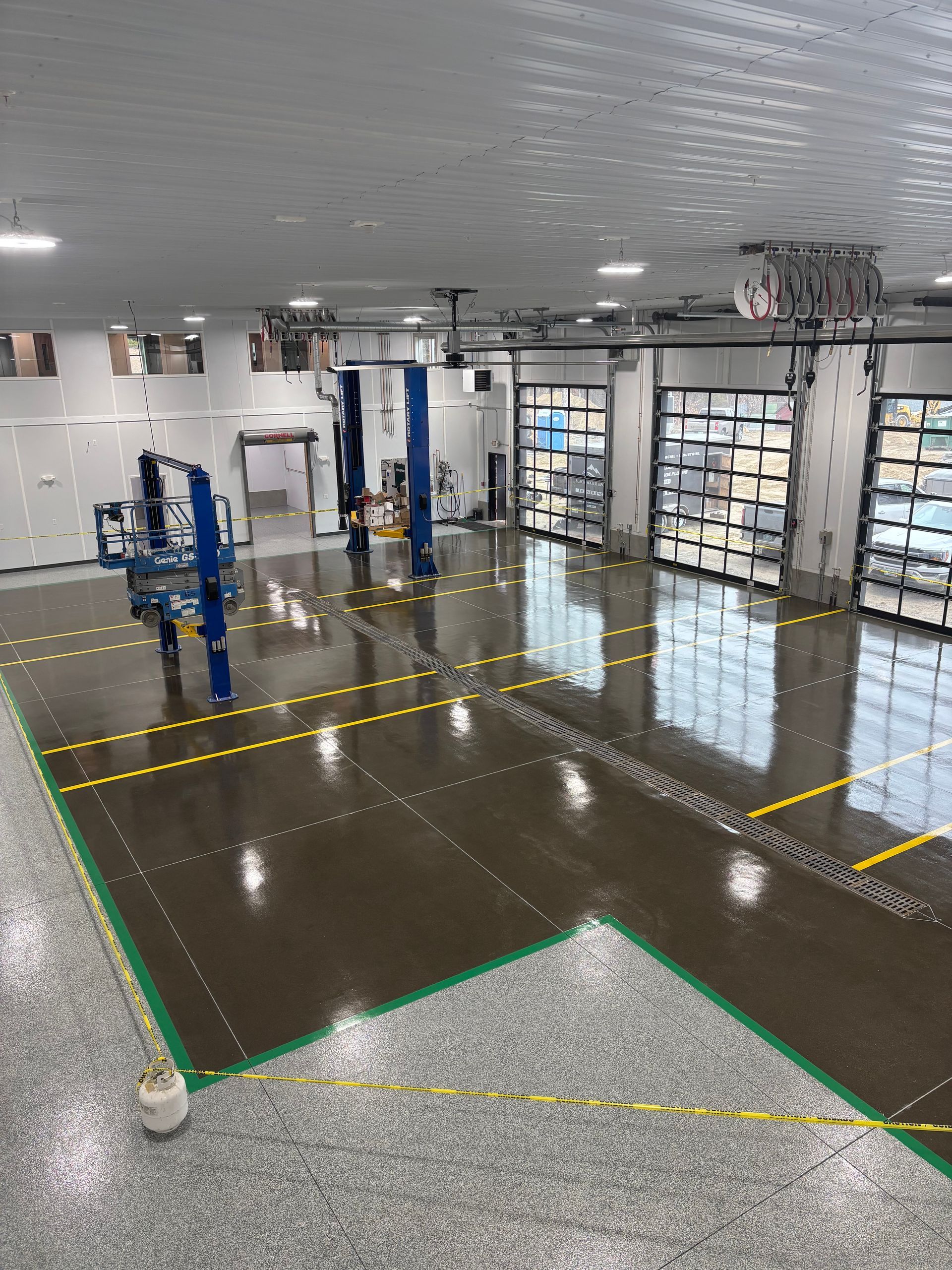 A large, bright auto repair shop with polished epoxy floor and vehicle lifts. Transparent garage doors let in light.