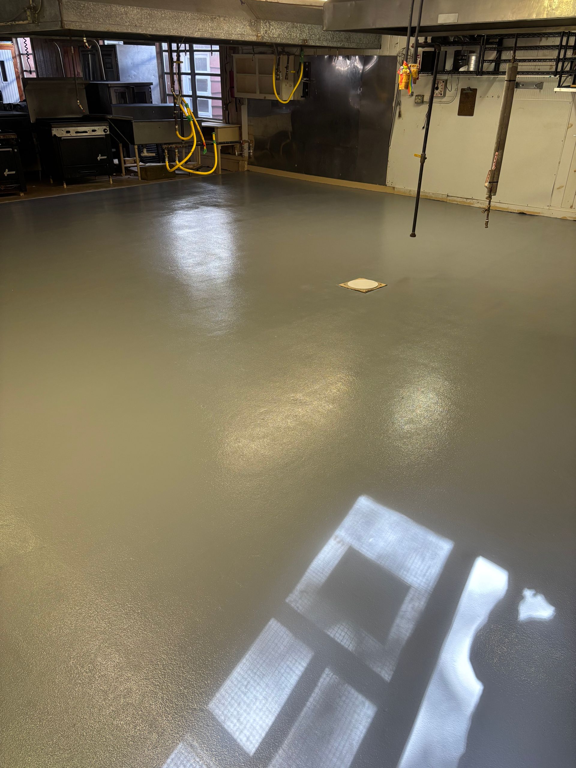 Gray epoxy floor with speckled finish in a basement, reflecting sunlight.