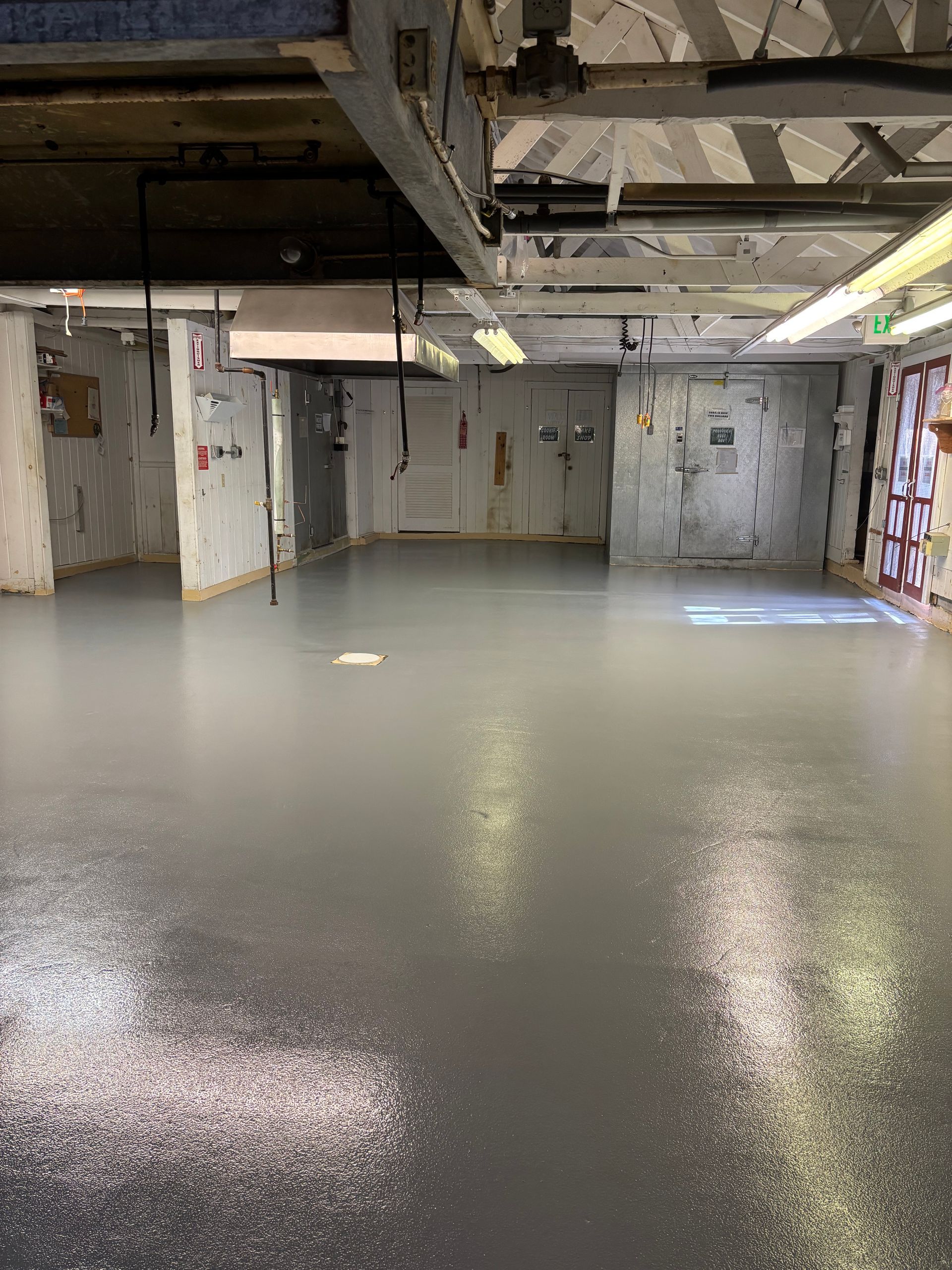Empty, gray-painted room with concrete walls, industrial ceiling, and a light-reflective floor.