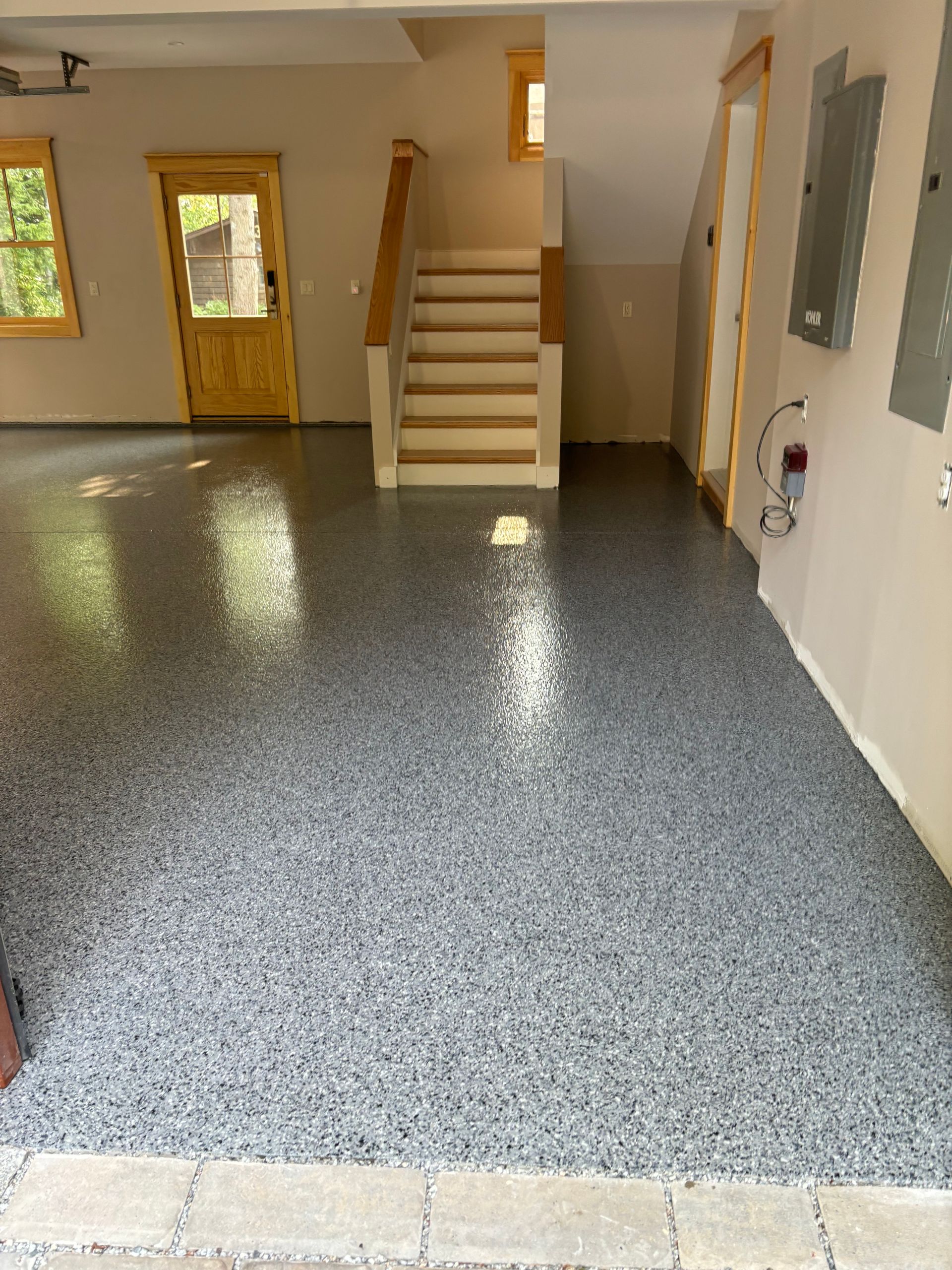 Garage with speckled gray epoxy floor, stairs, and a wooden door.