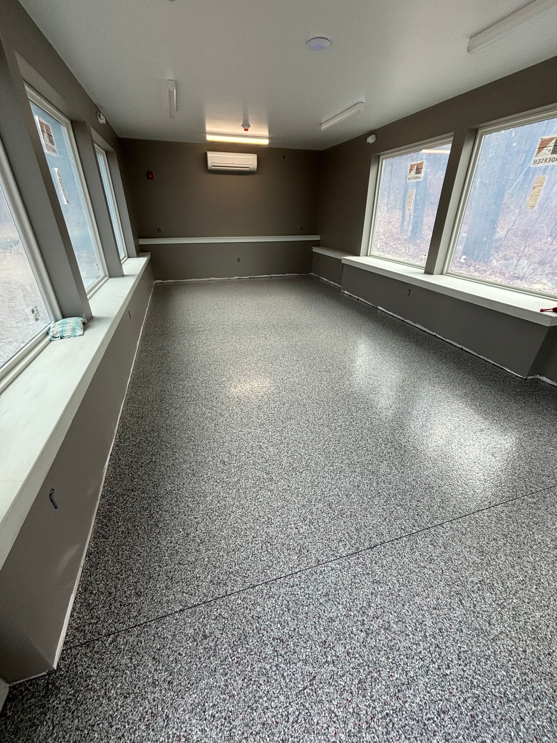 Empty room with speckled grey floor, windows, and built-in benches.