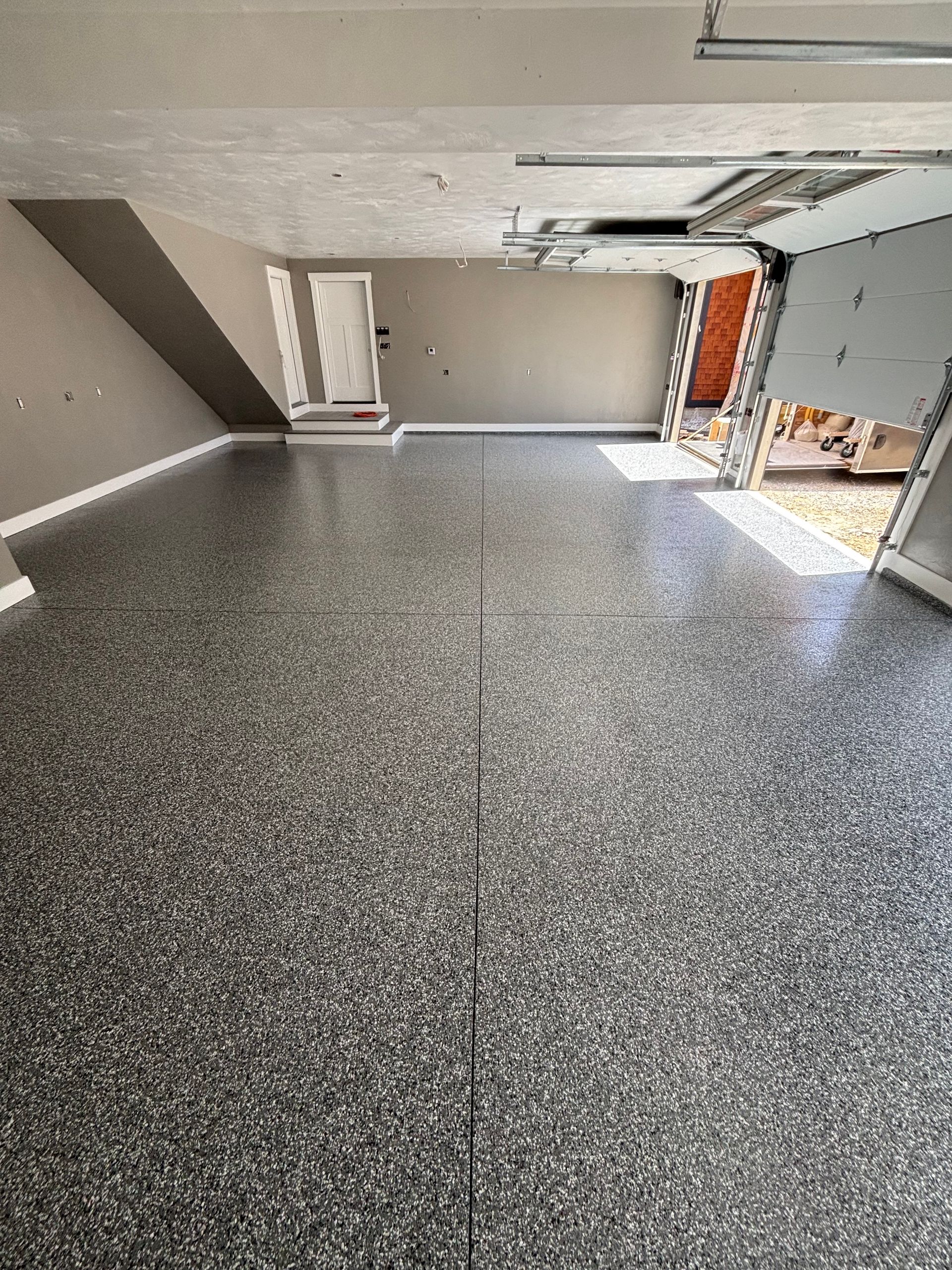 Empty garage with speckled, gray floor, beige walls, and open garage door.