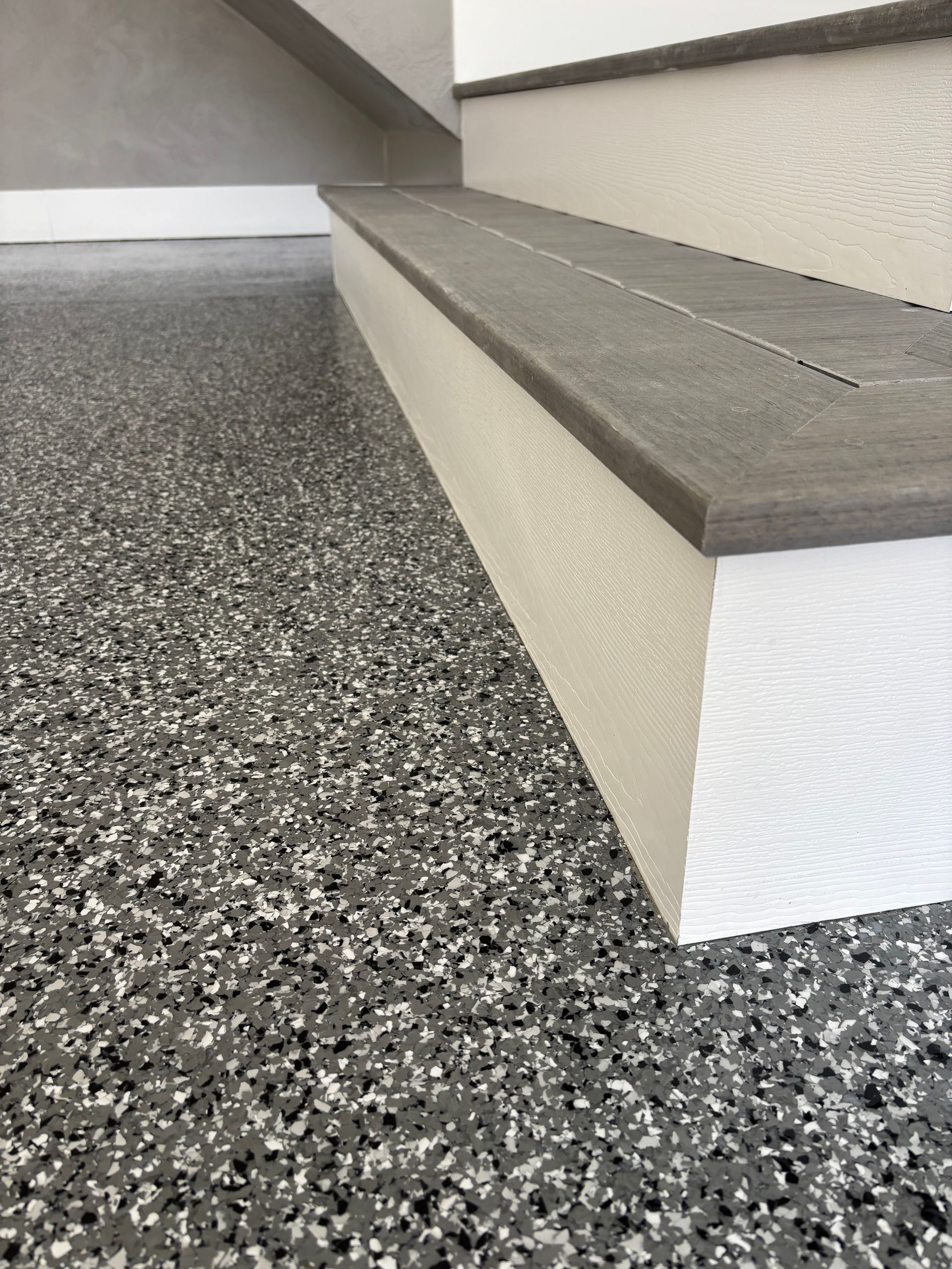 Staircase with gray and white flecked flooring, light gray steps, and white risers.
