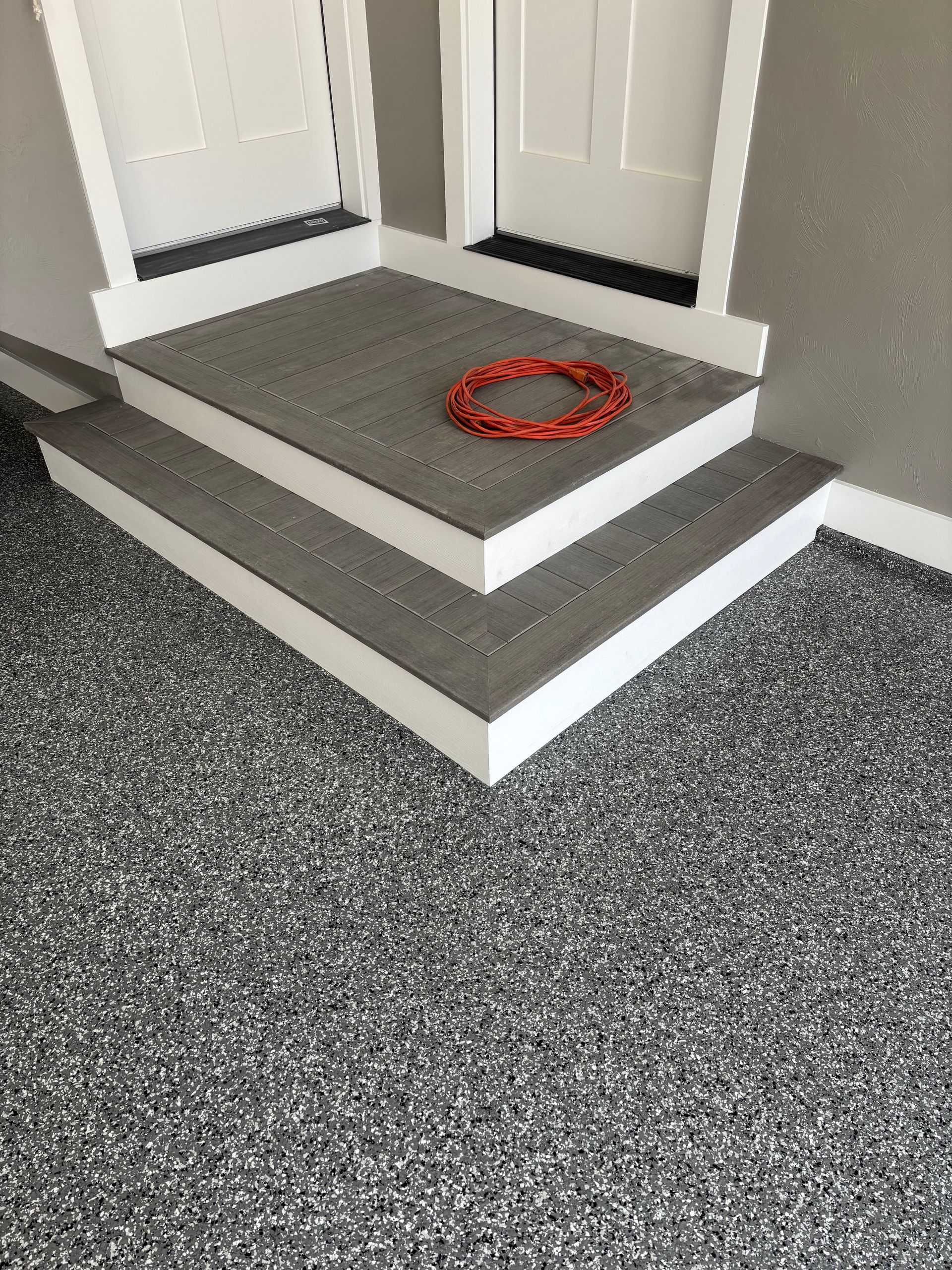 Grey flecked flooring with two steps leading to a white door frame and an orange pet toy.