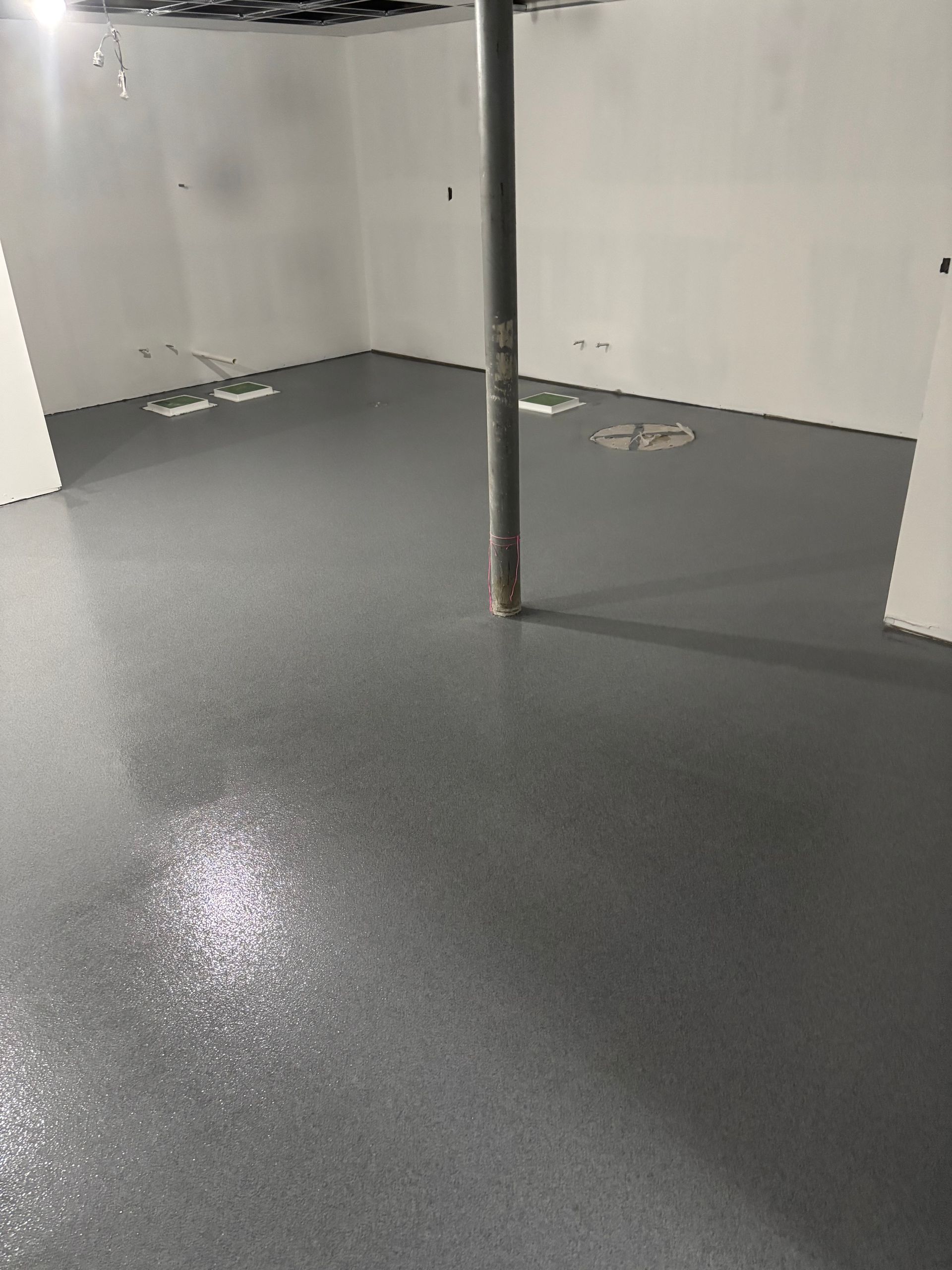 Gray epoxy floor in a basement with a metal pipe and white walls.