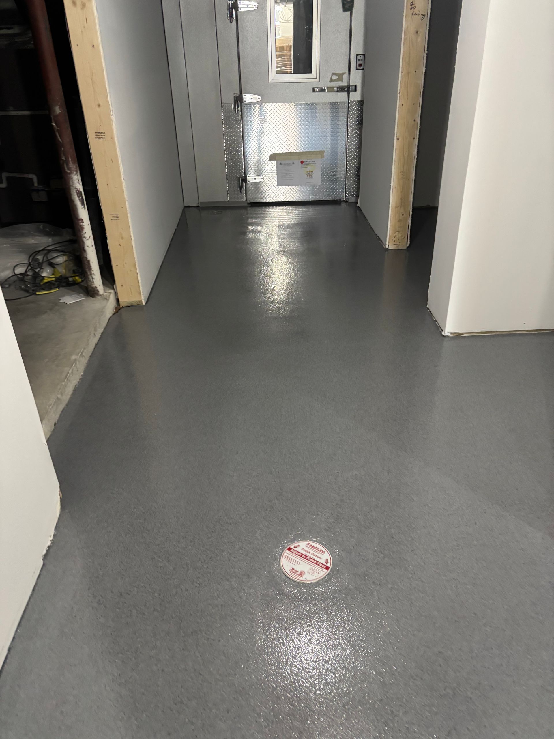 Gray-painted concrete floor in a hallway with a drain cover; bare framing at doorways.