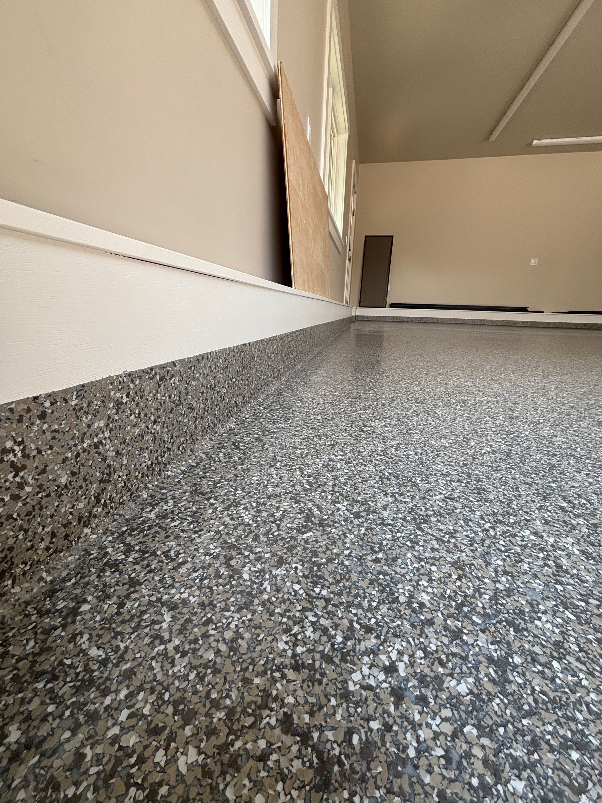 Close-up of a speckled, gray epoxy floor, baseboard, and walls of a room with a doorway and window.