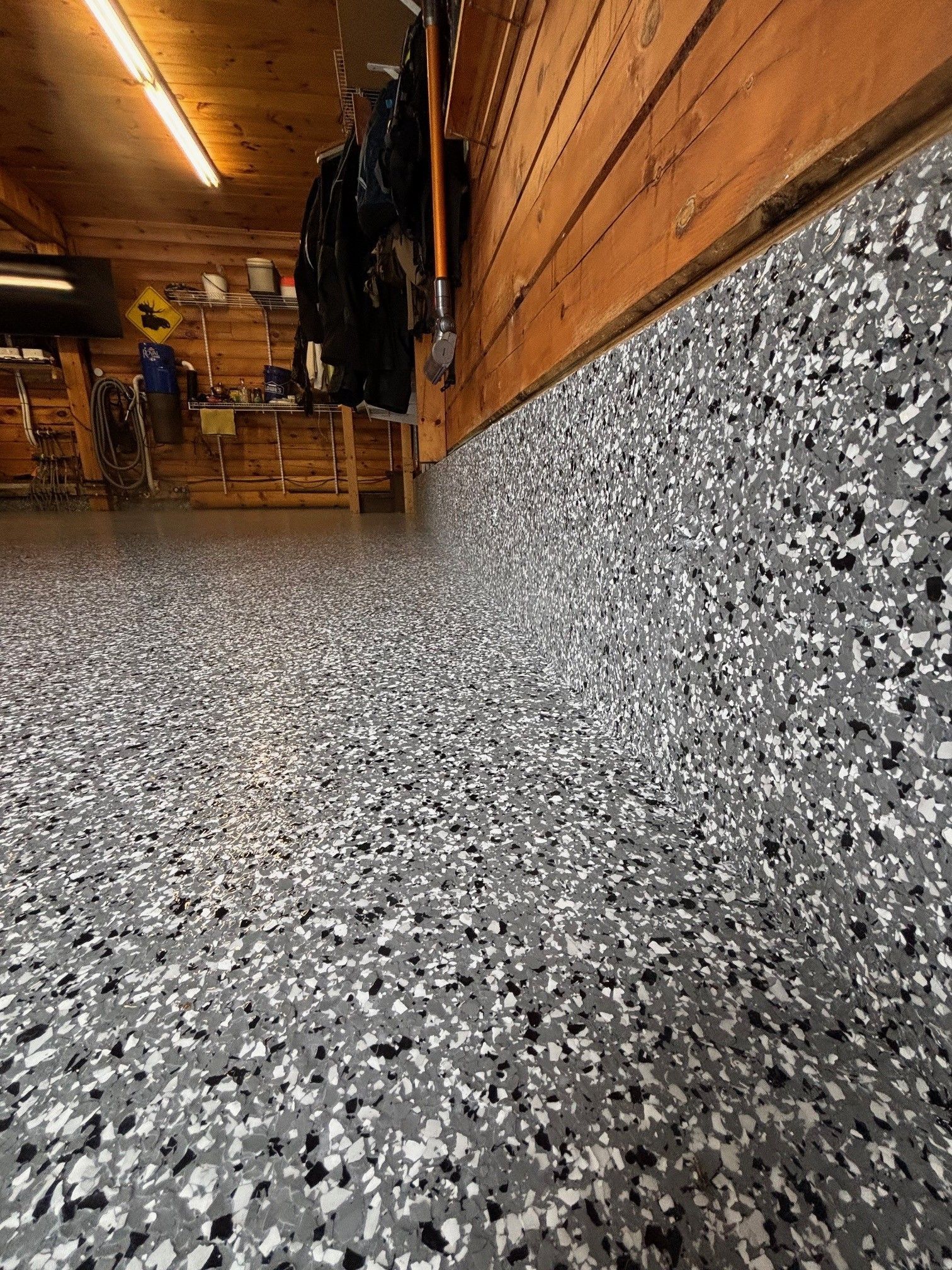 Garage floor with gray, black, and white speckled epoxy coating, bordering wooden wall.