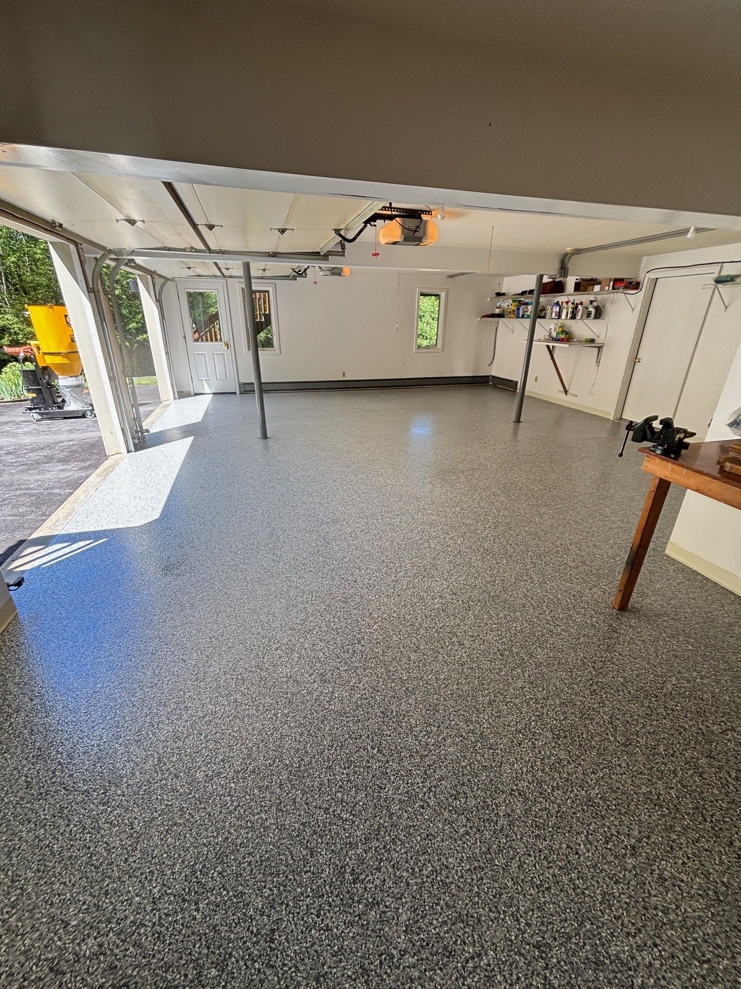 Spacious garage with epoxy flooring, open garage door. White walls, overhead door opener, shelves on the wall.