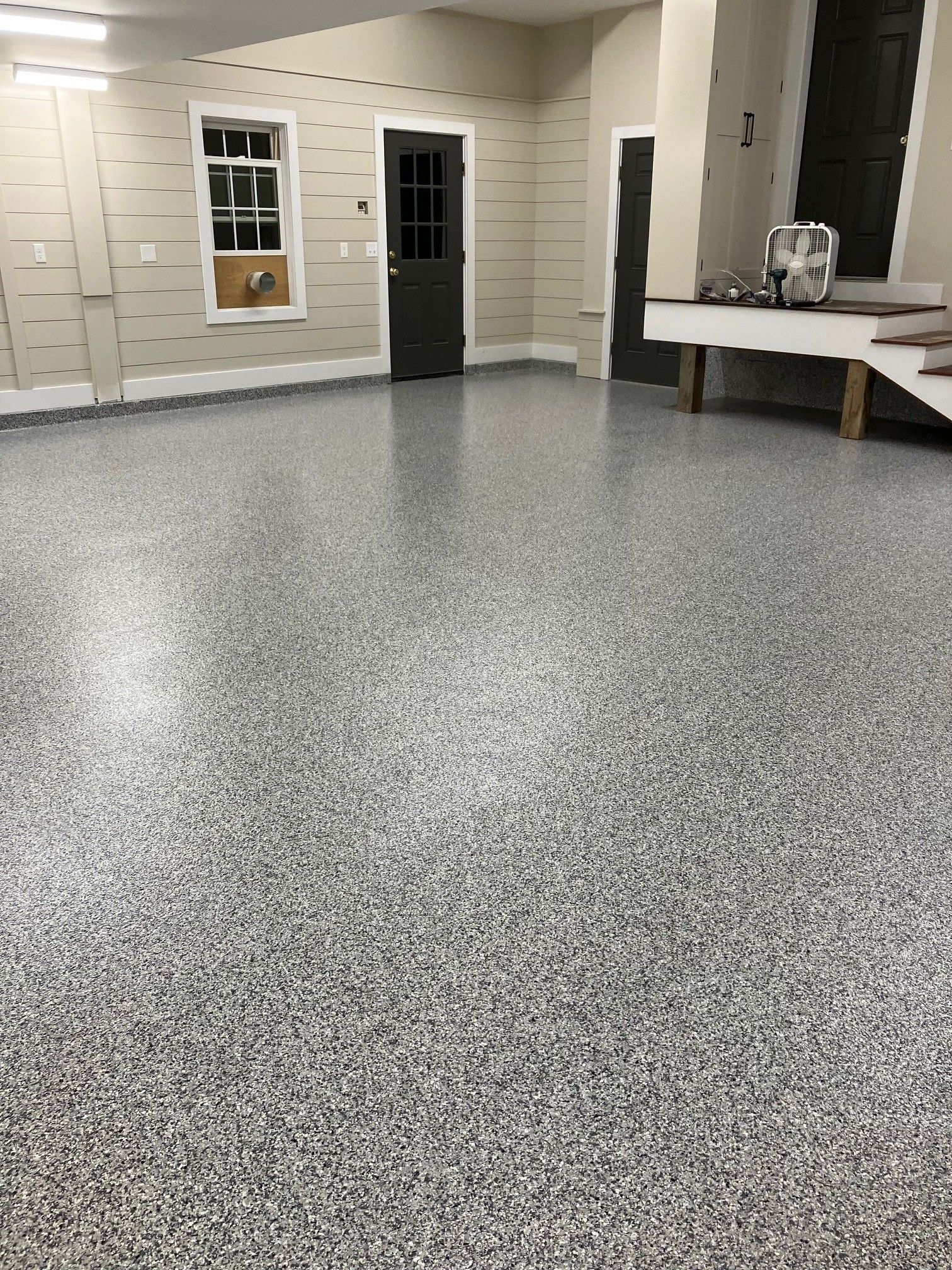 Garage with speckled gray flooring, door, window, and work table.