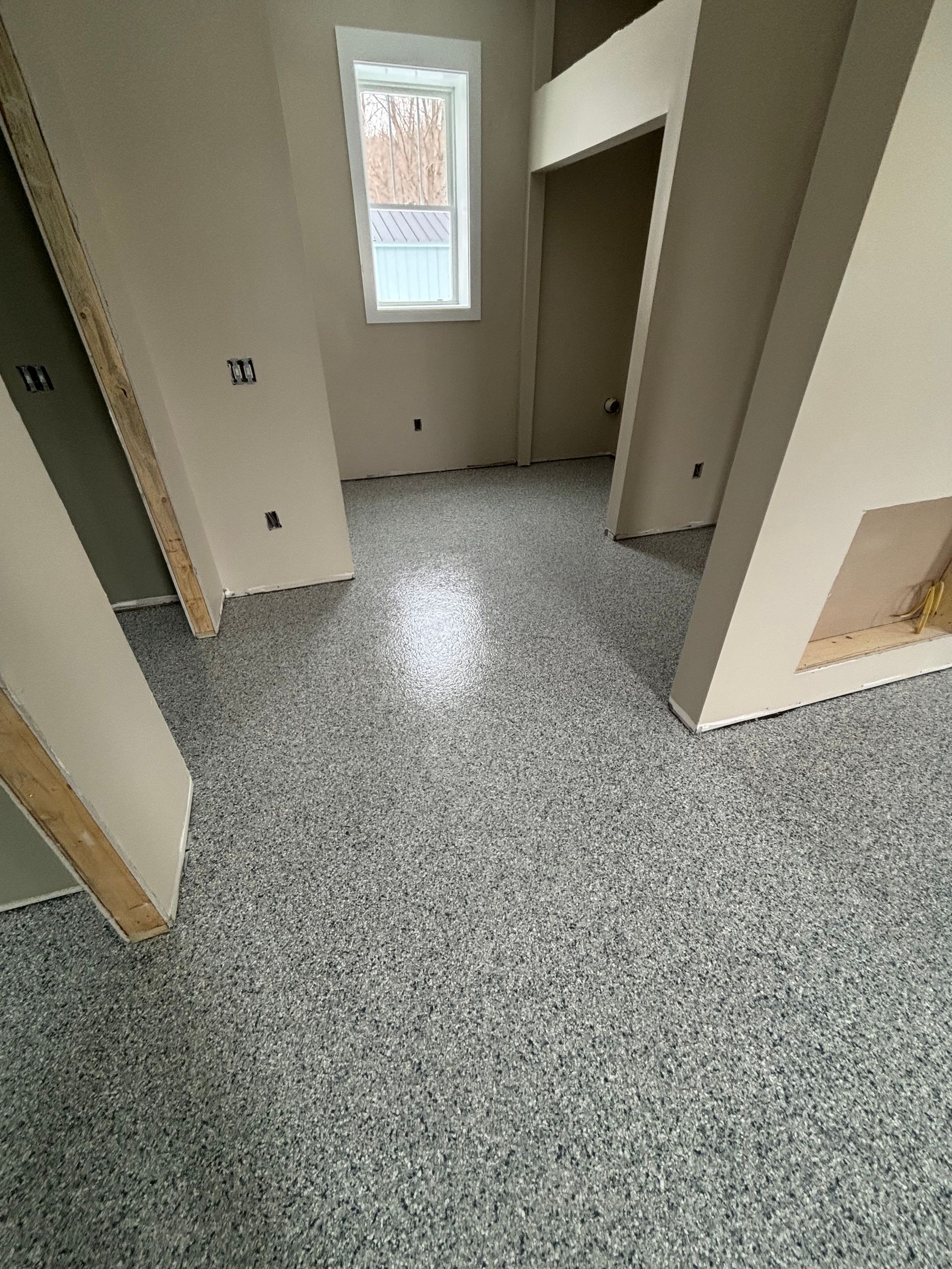 Room interior with mottled gray flooring, beige walls, and window.