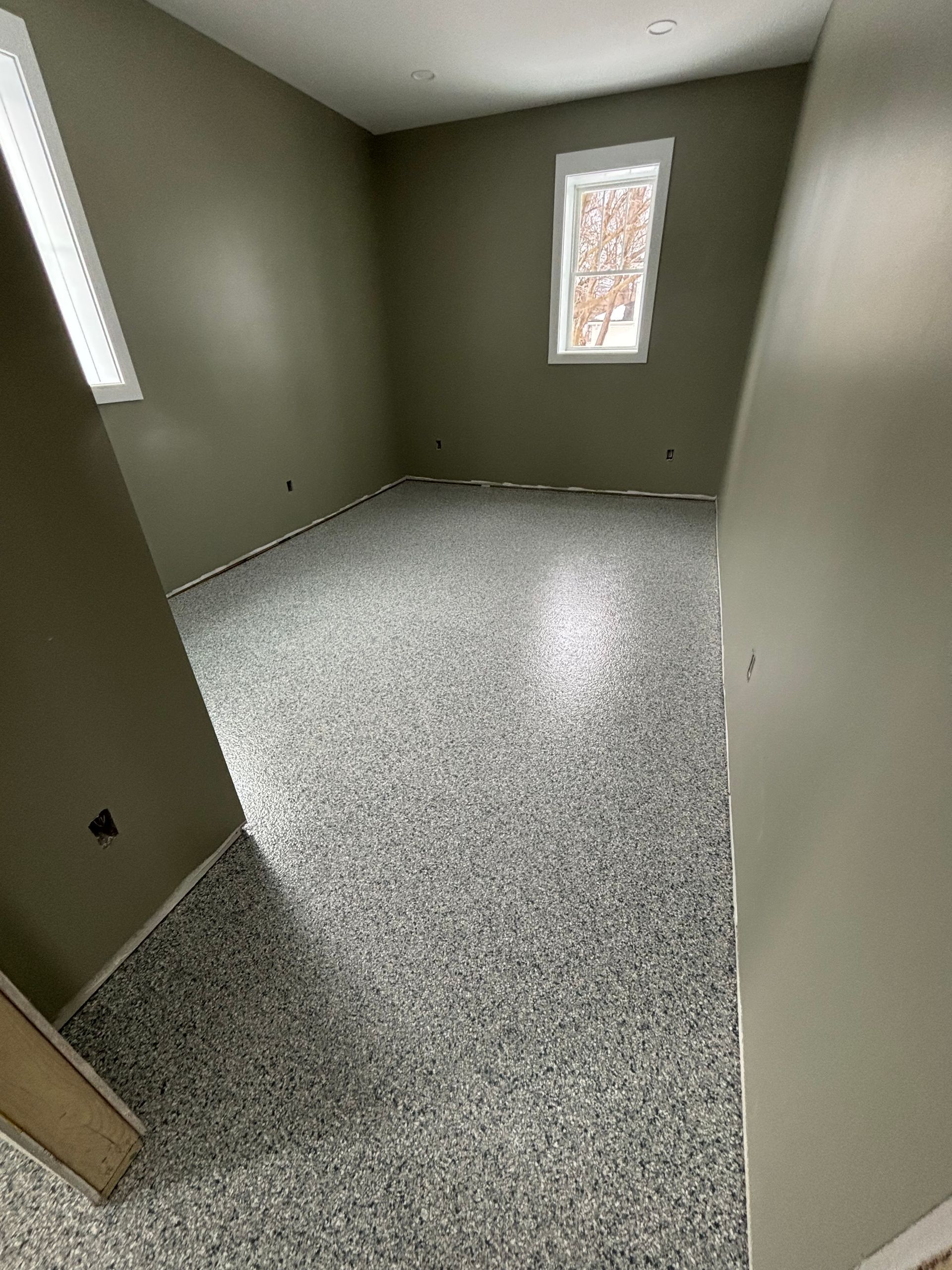 Empty room with gray speckled flooring and pale green walls, with two windows.