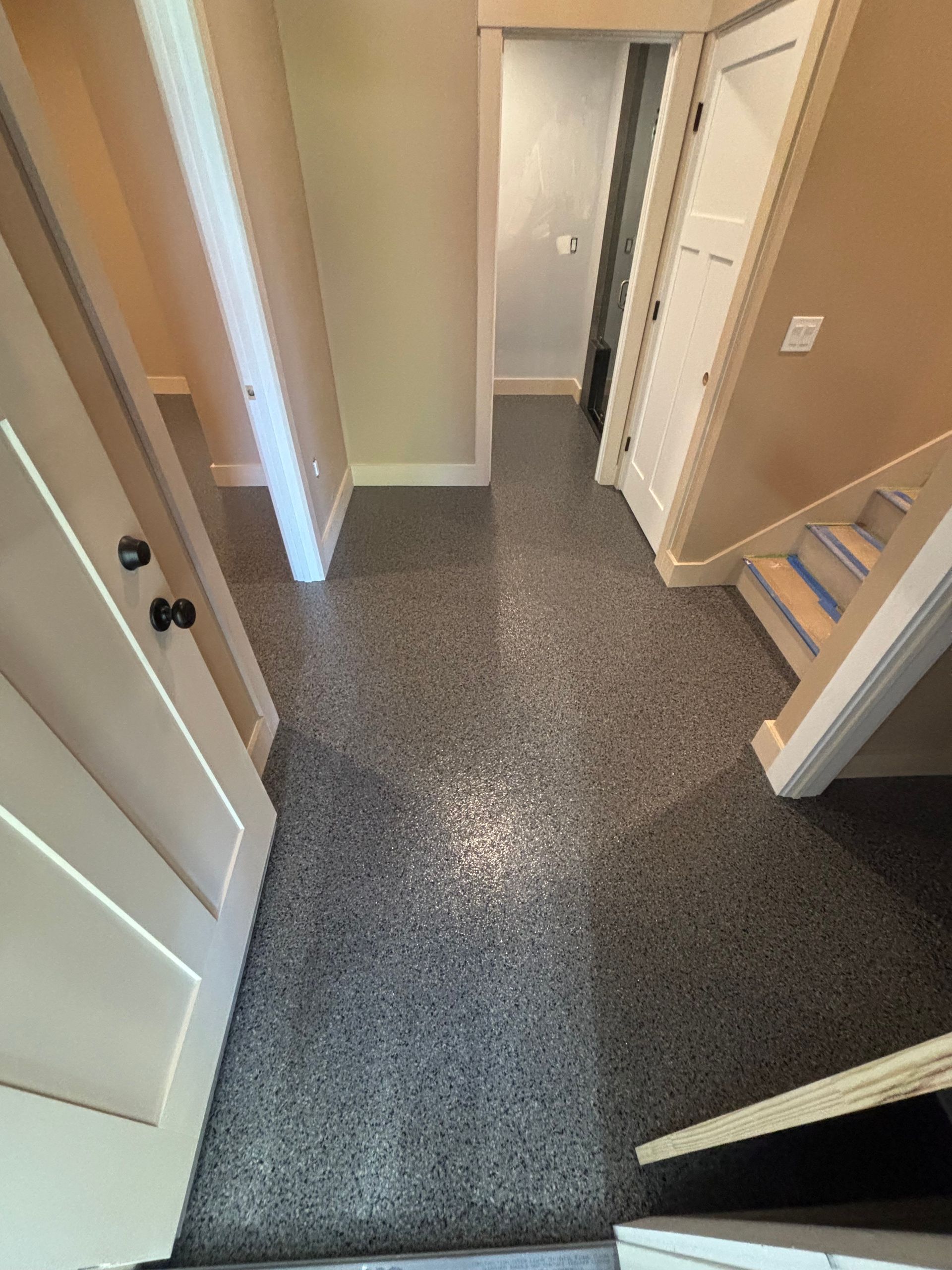 Hallway with speckled gray flooring, cream doors, and a staircase.