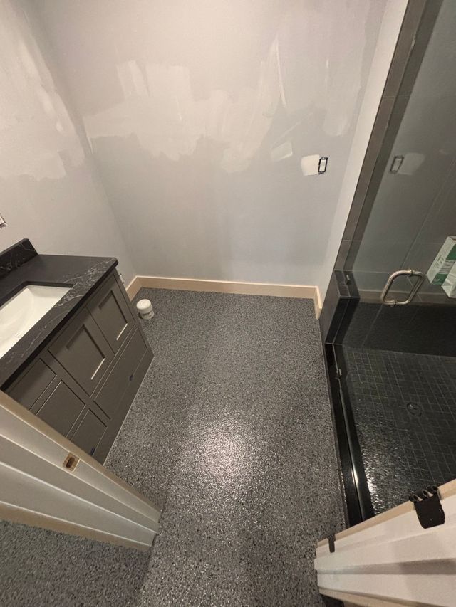 Bathroom with gray epoxy floor, gray vanity, and glass shower.