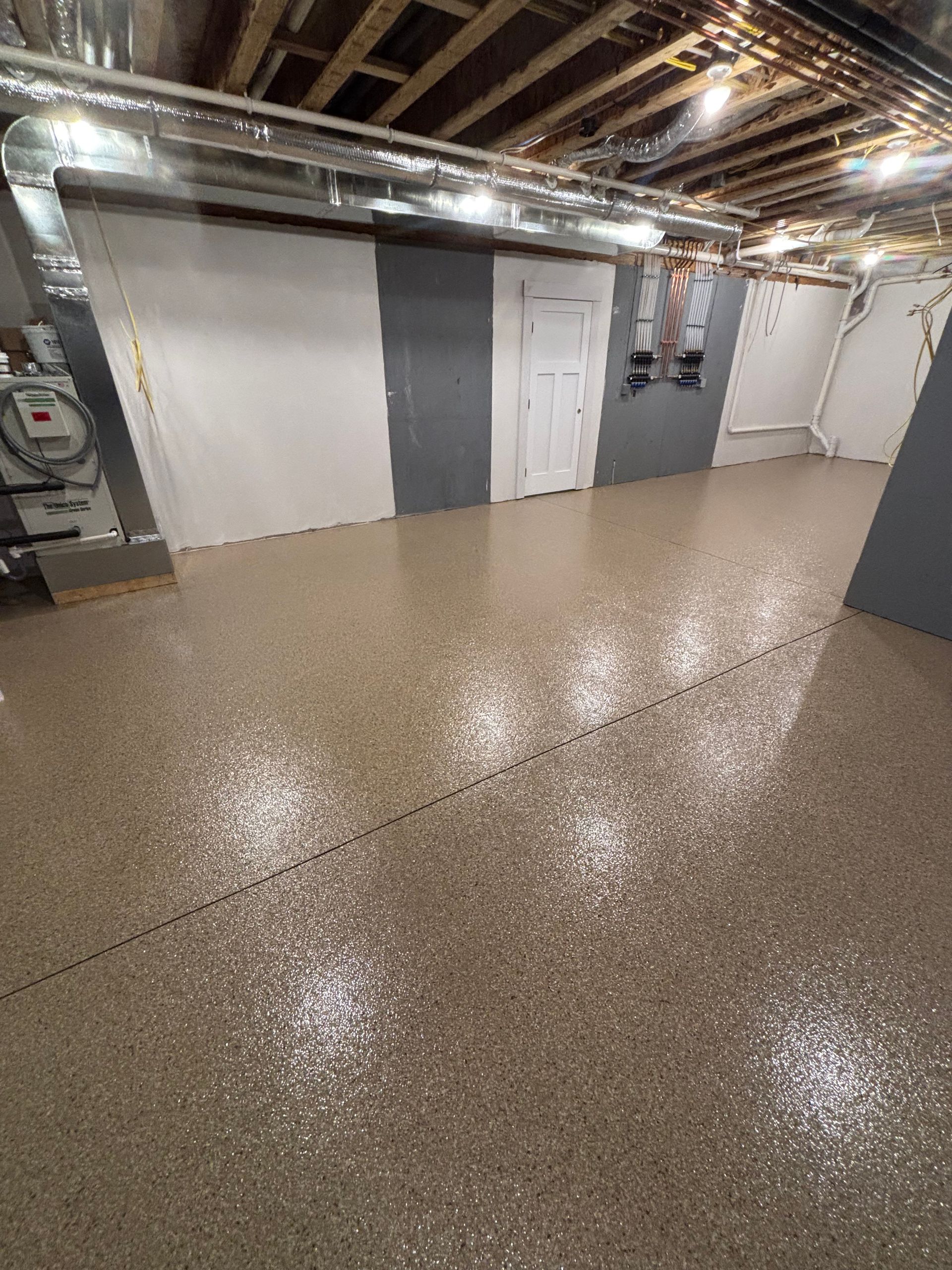 Basement with shiny, speckled tan epoxy floor. White and gray walls, ductwork, and closed white door.