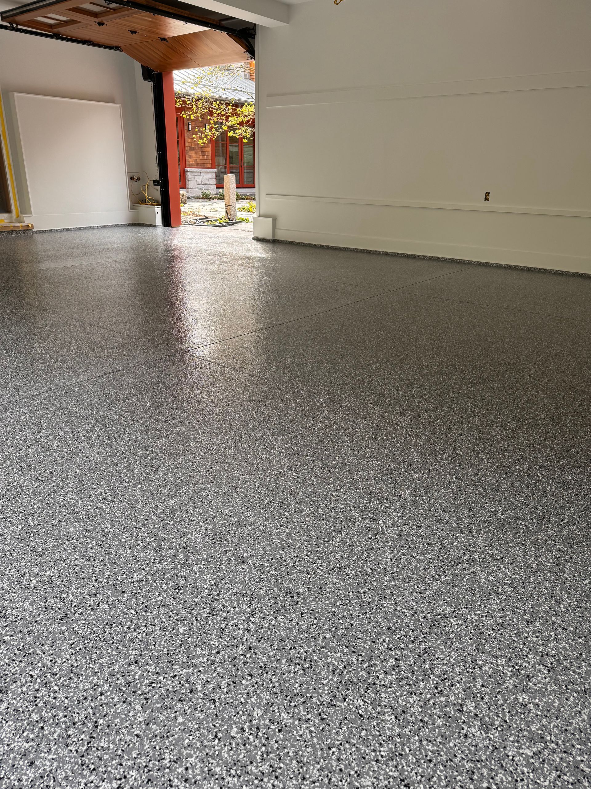 Gray and white speckled epoxy floor in a garage with open door to outside.