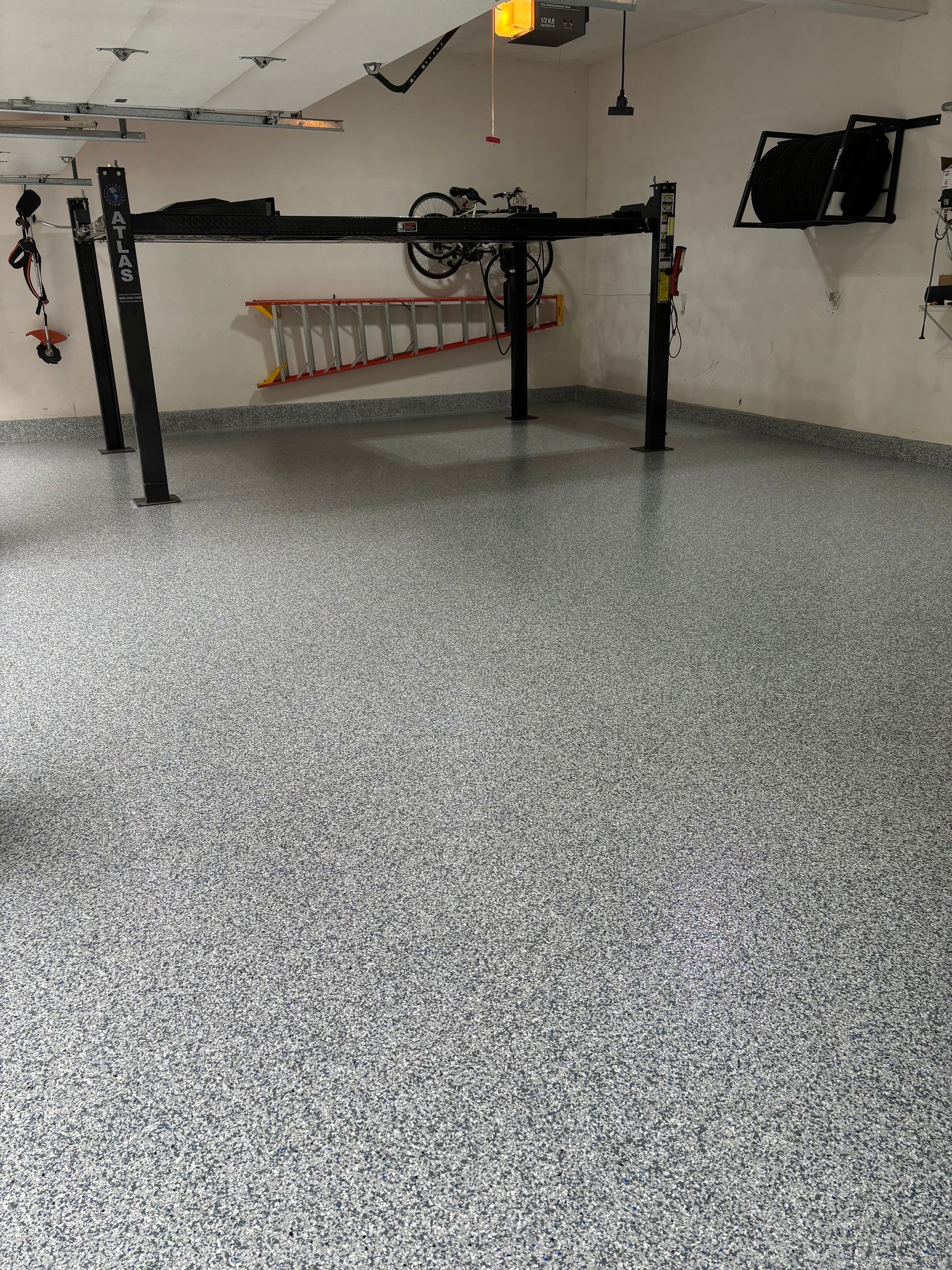 Garage with speckled gray flooring, car lift, and tools on the wall.