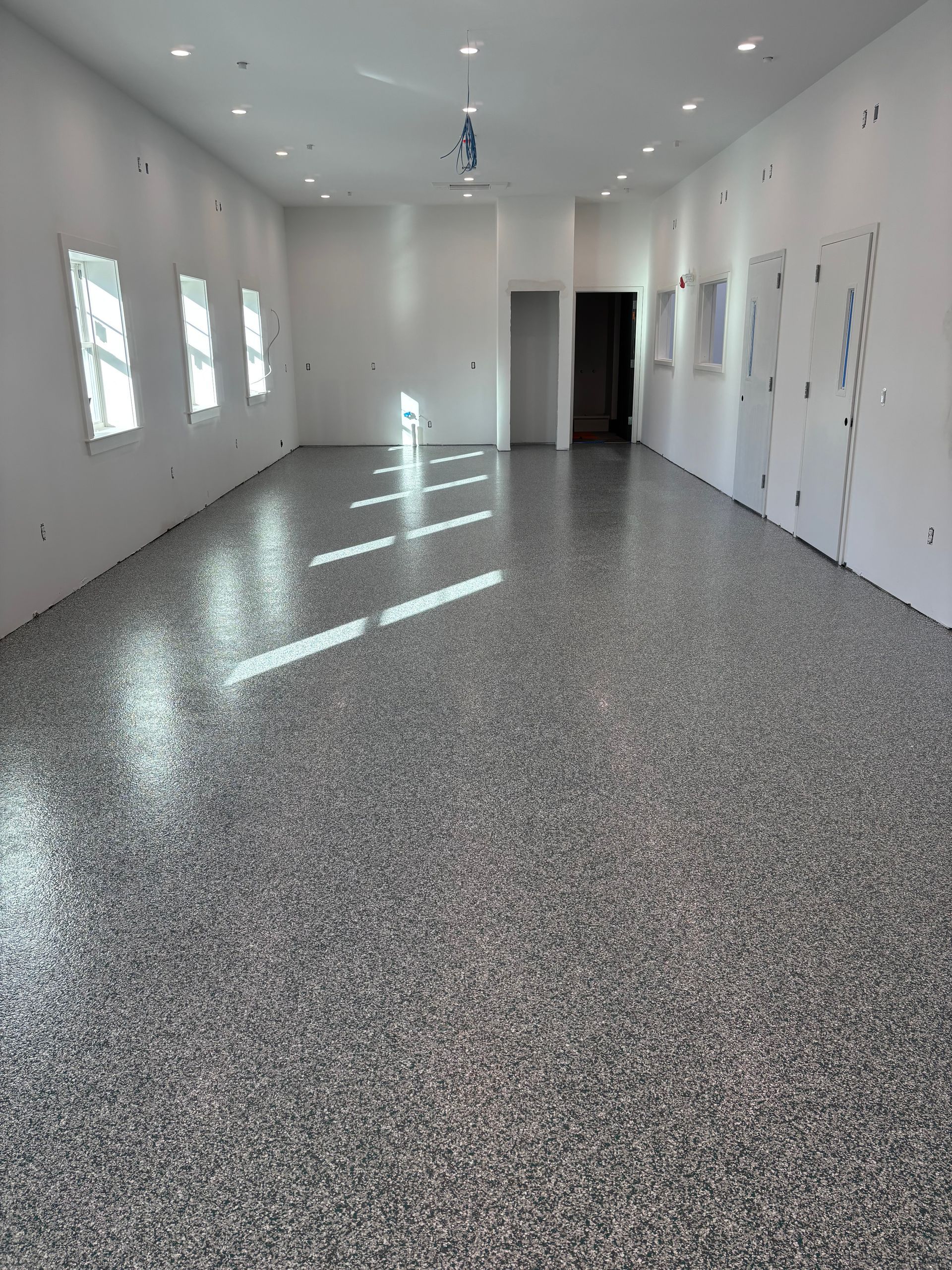 Empty room with a speckled gray epoxy floor, white walls, and small windows.