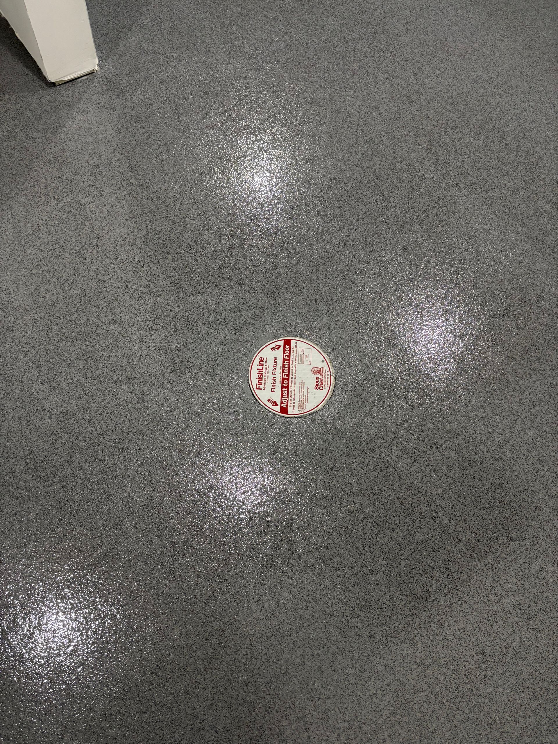 Gray speckled epoxy floor with a round drain cover; three bright light reflections.