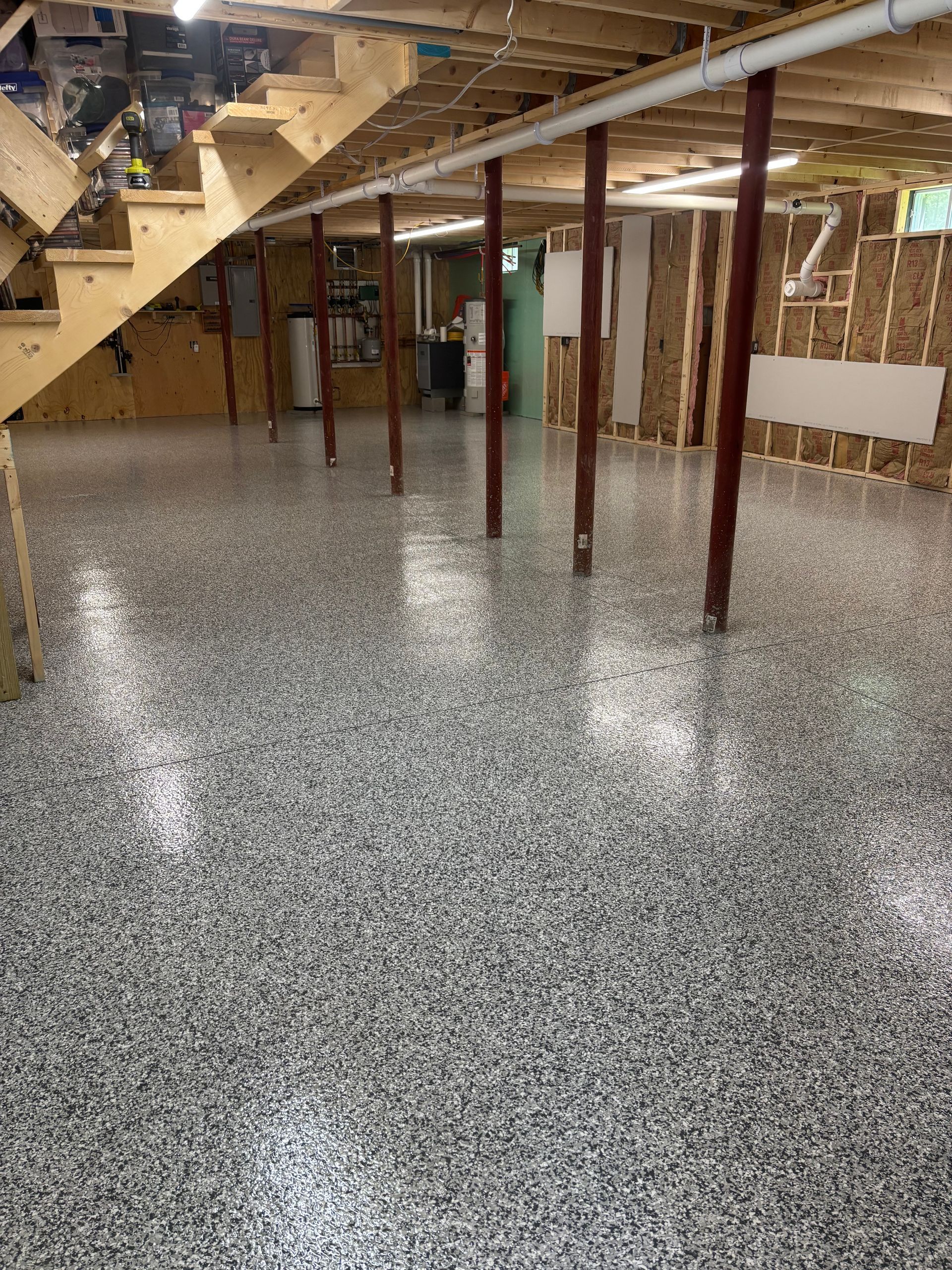 Finished basement with gray speckled epoxy floor and wooden support beams.