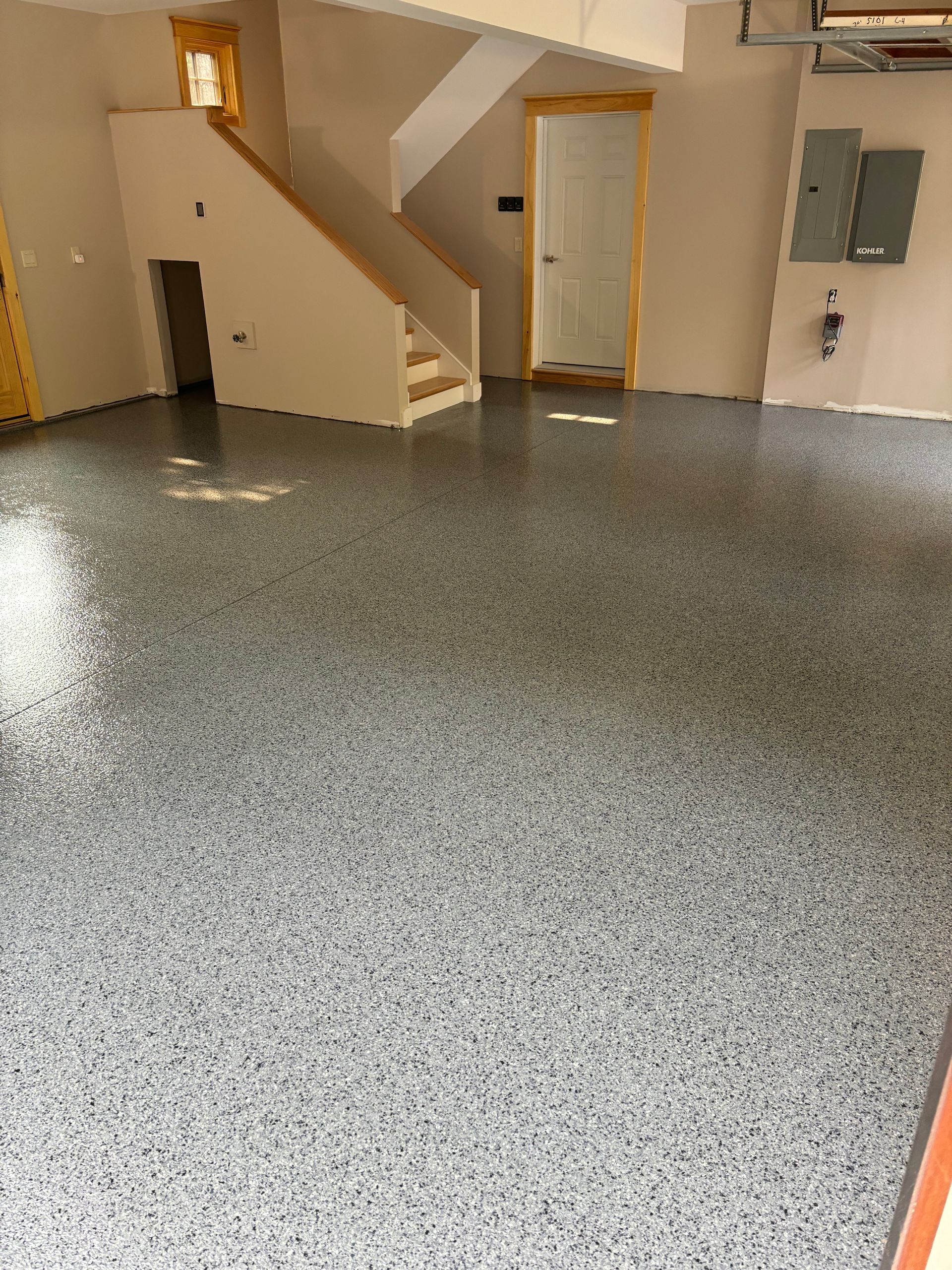 A garage interior with a speckled epoxy floor, stairs, and a door.