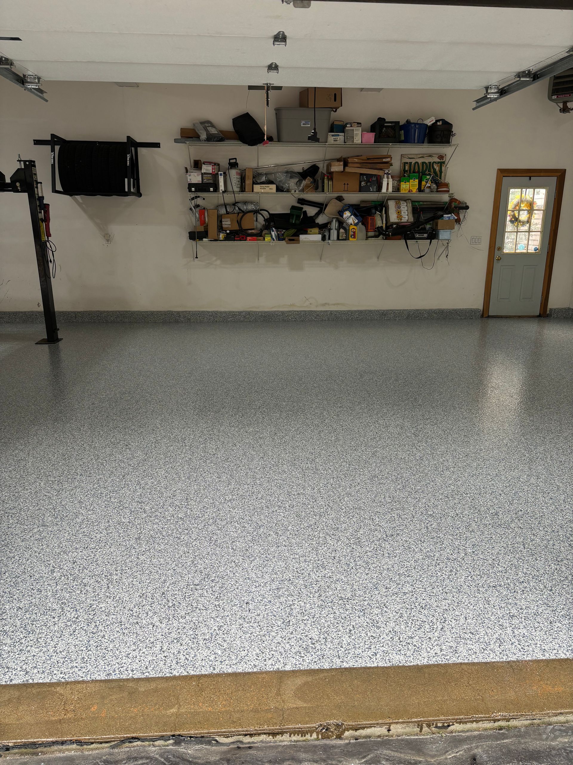 Garage with gray speckled epoxy floor, white walls, and a shelf of items.