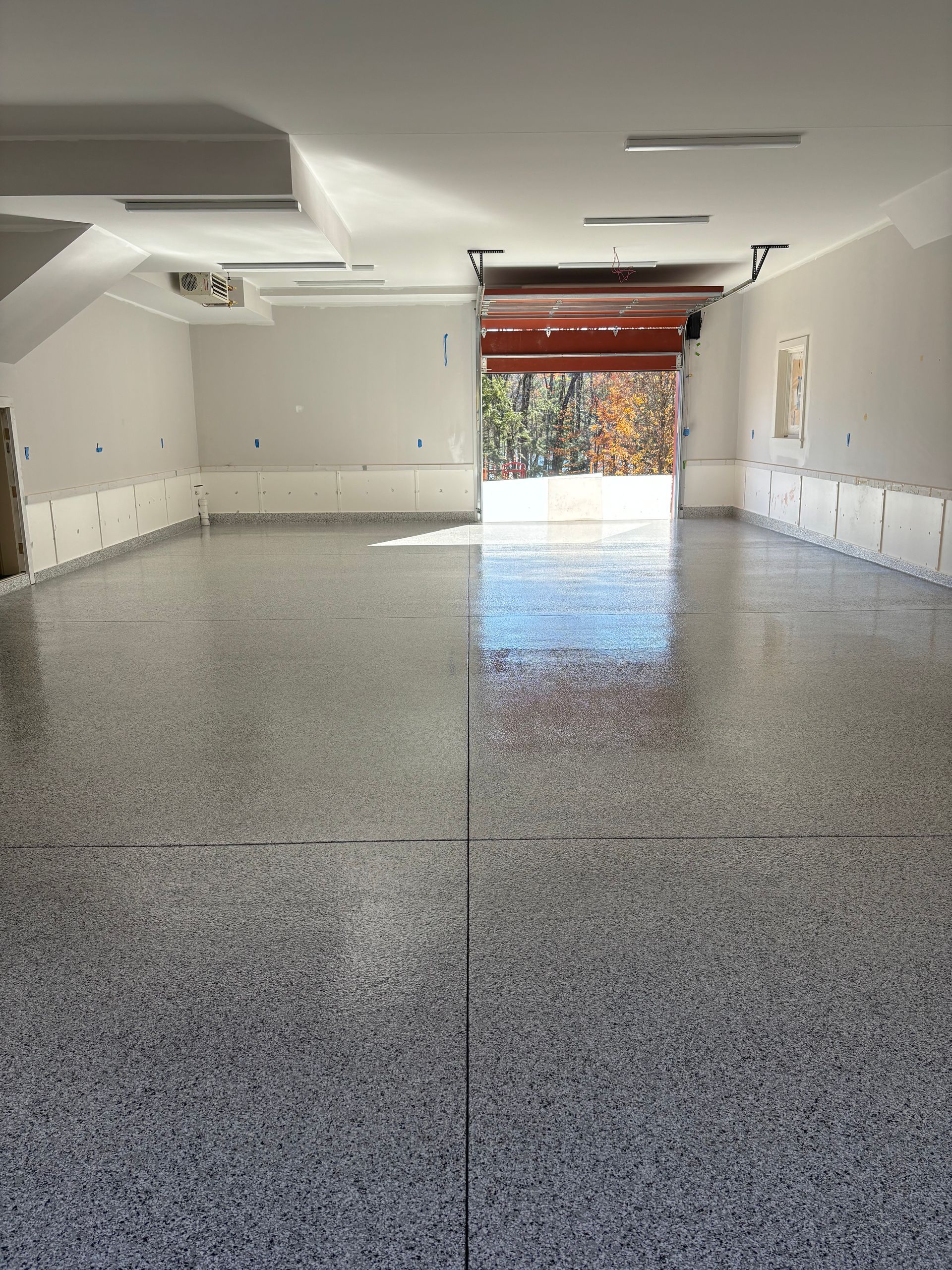 Empty garage with speckled, glossy floor and open garage door.