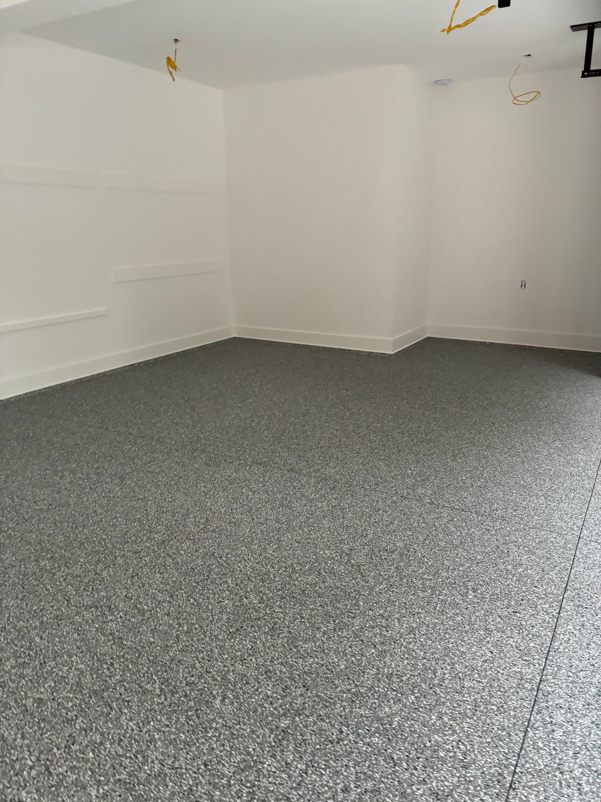 Gray speckled epoxy floor in a white-walled room with exposed wiring on the ceiling.