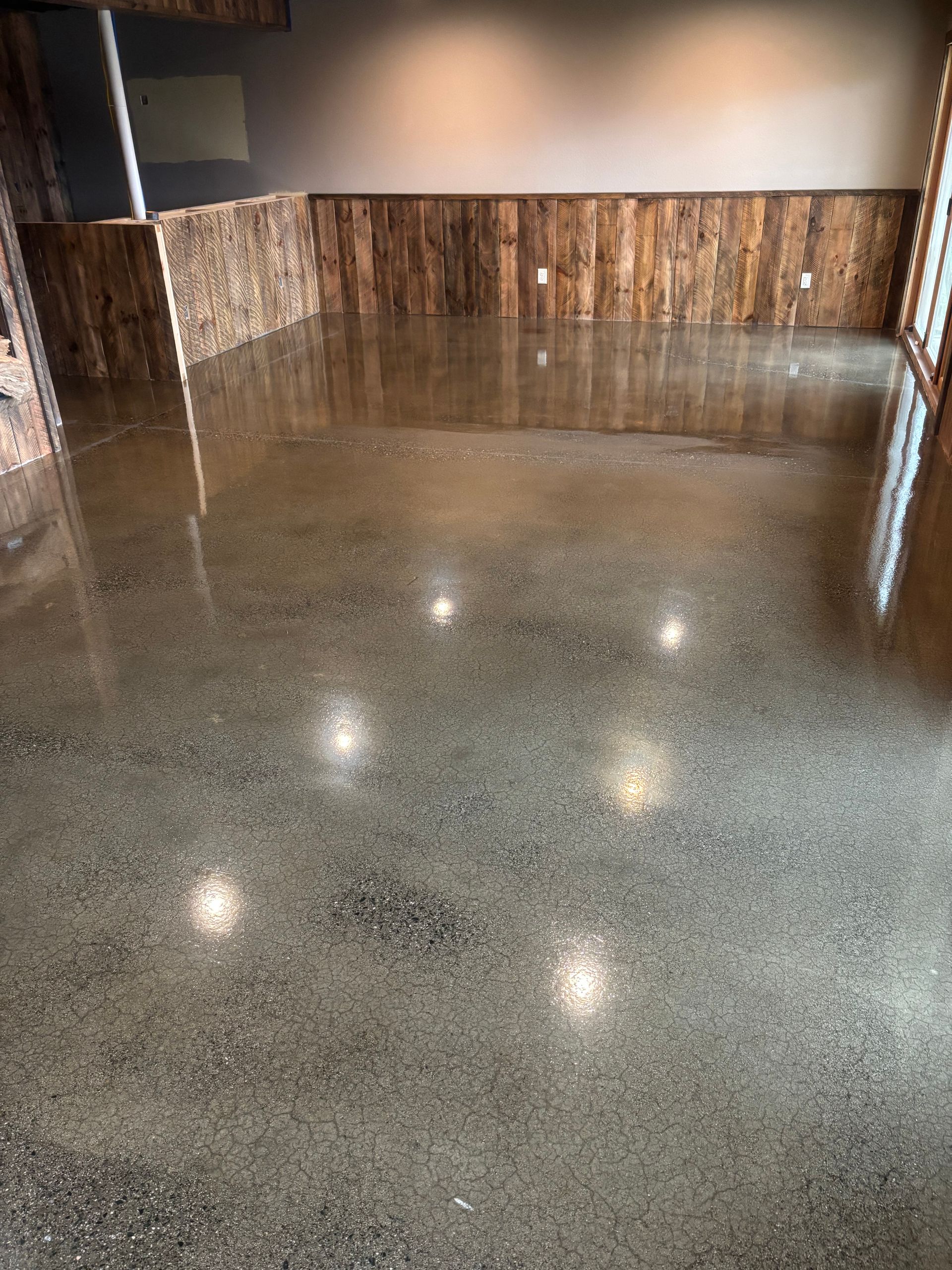 Polished concrete floor reflecting ceiling lights in a room with wood paneling on the walls.