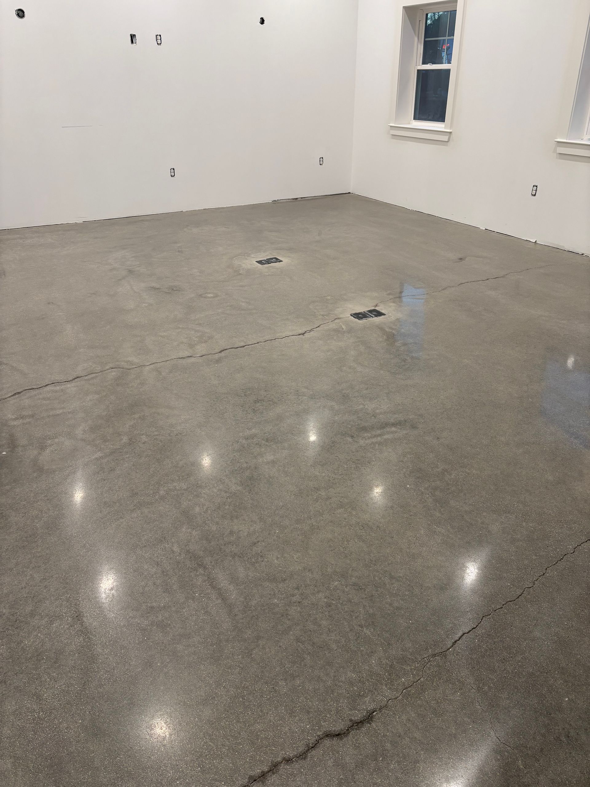 Polished concrete floor in an empty room, cracks visible, white walls, two windows.