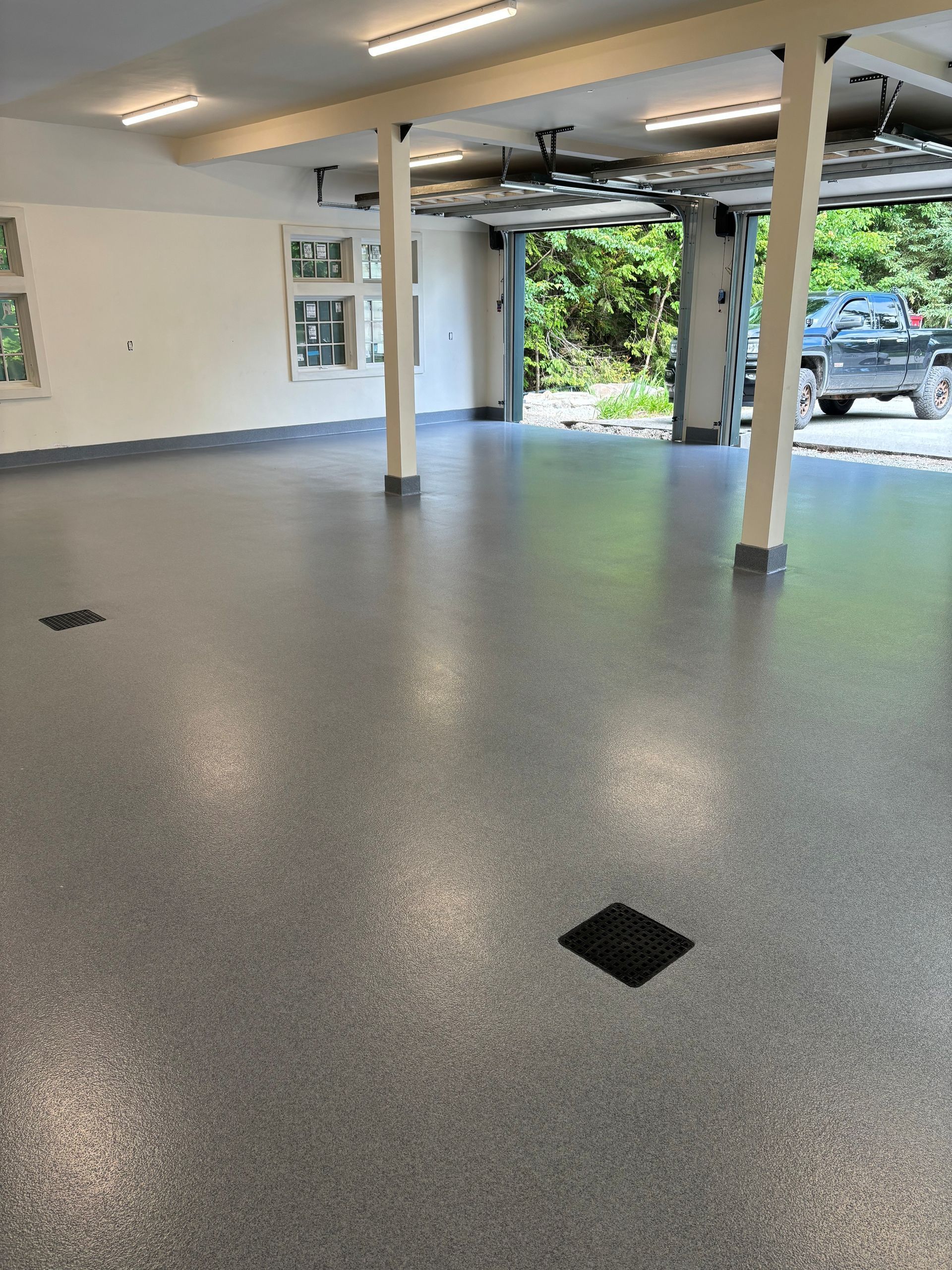 Gray speckled epoxy garage floor, open garage door, supporting columns, overhead lights.