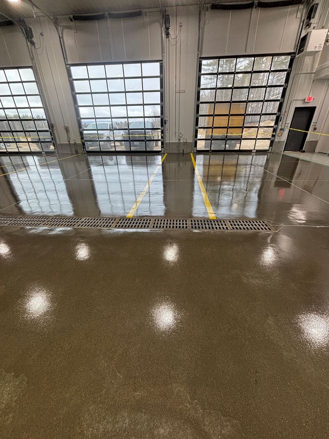 Interior of a garage with large glass doors reflecting the outside. A polished concrete floor has yellow lines.