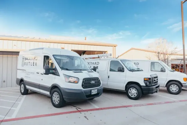 Three white work vans parked in a row on a concrete lot in front of a building under a bright blue sky.