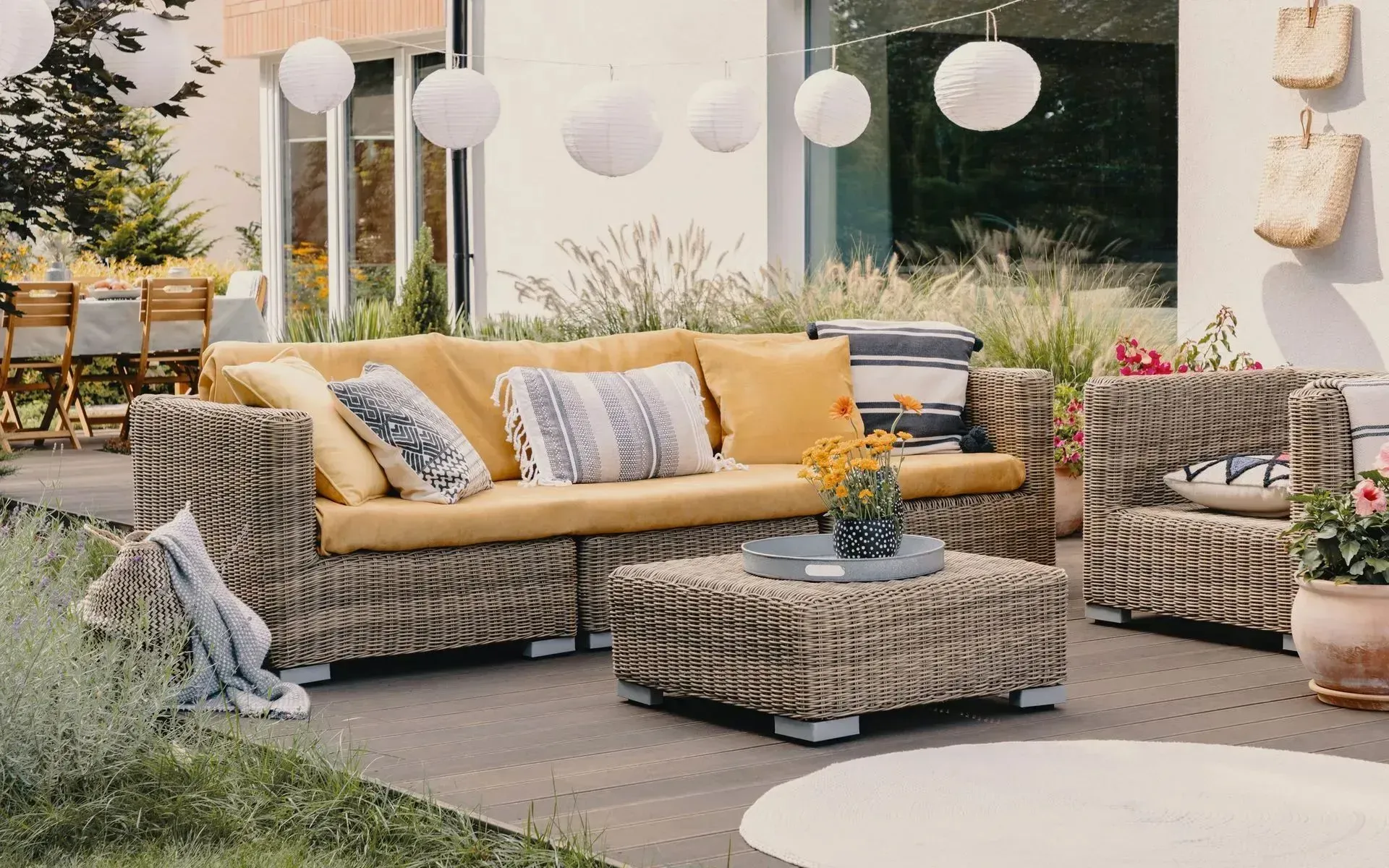 Wicker outdoor sofa and matching armchair with mustard-yellow cushions on a patio with decorative hanging lanterns.